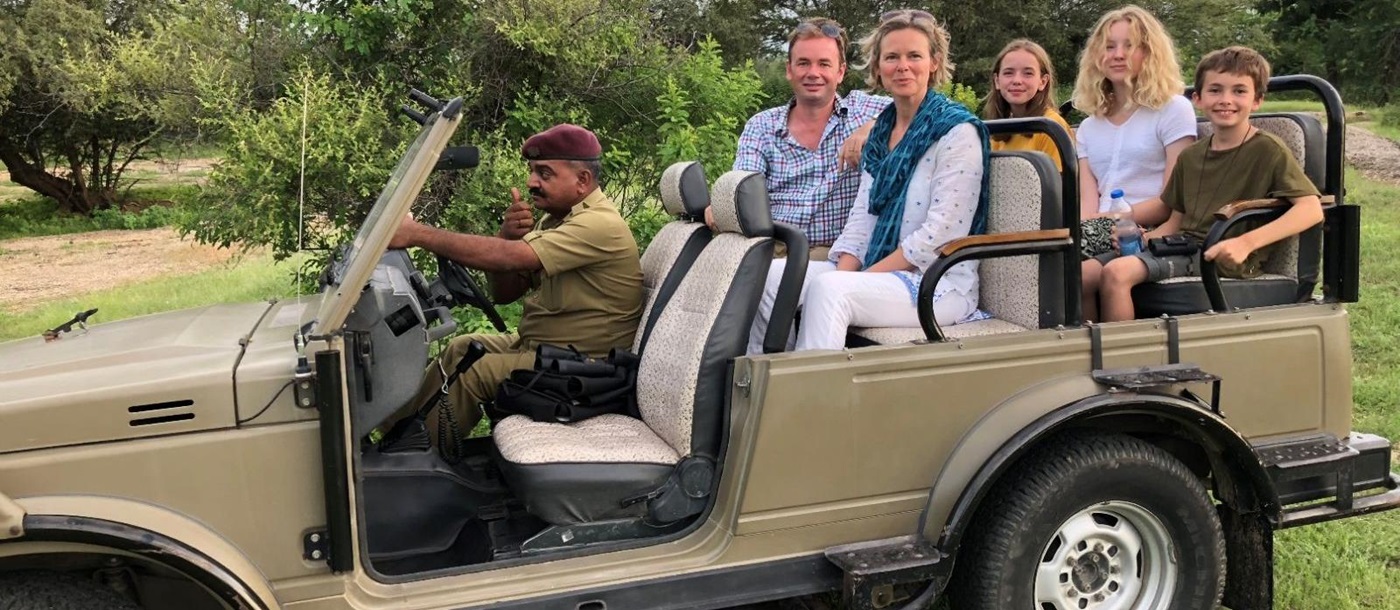 A family of two adults and three children sitting in a safari jeep with a driver in India