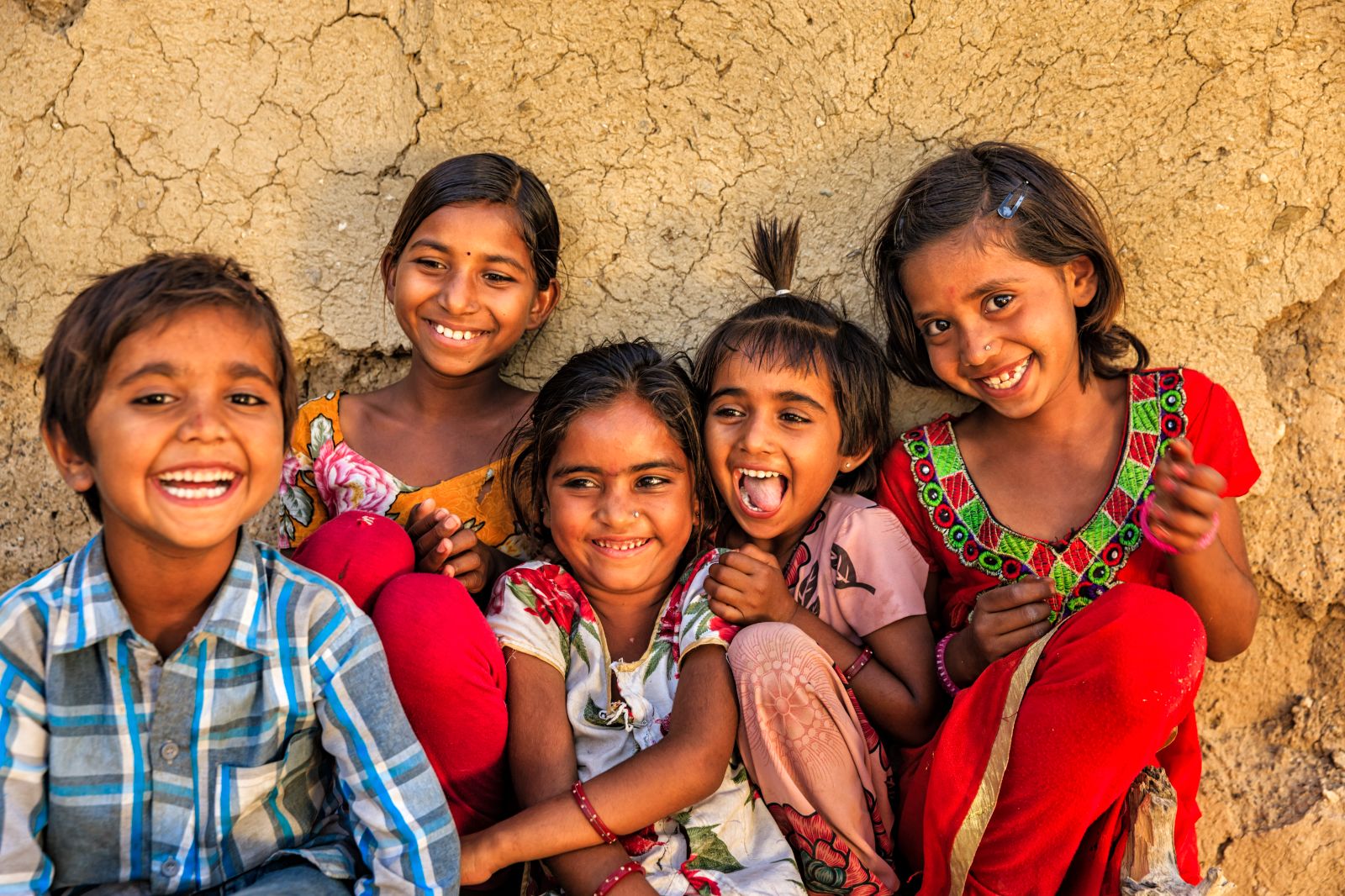 Smiling children standing in front of a mud wall in India