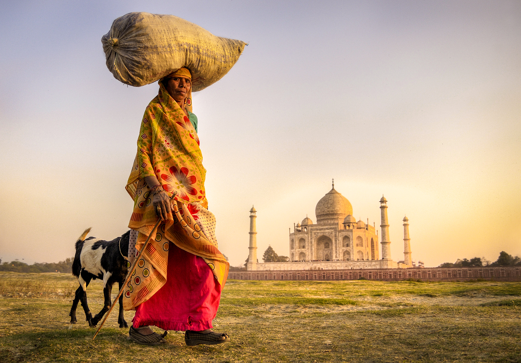 A woman carrying supplies on her head in front of the Taj Mahal