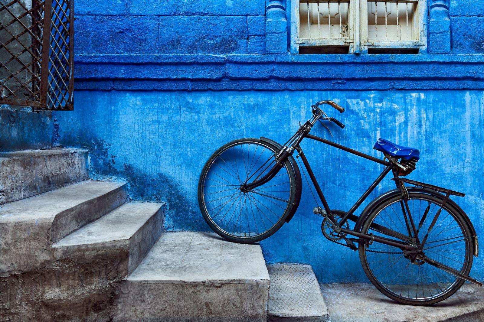 A bike with its front wheel on a step leaning up against a blue wall in Jodhpur in India