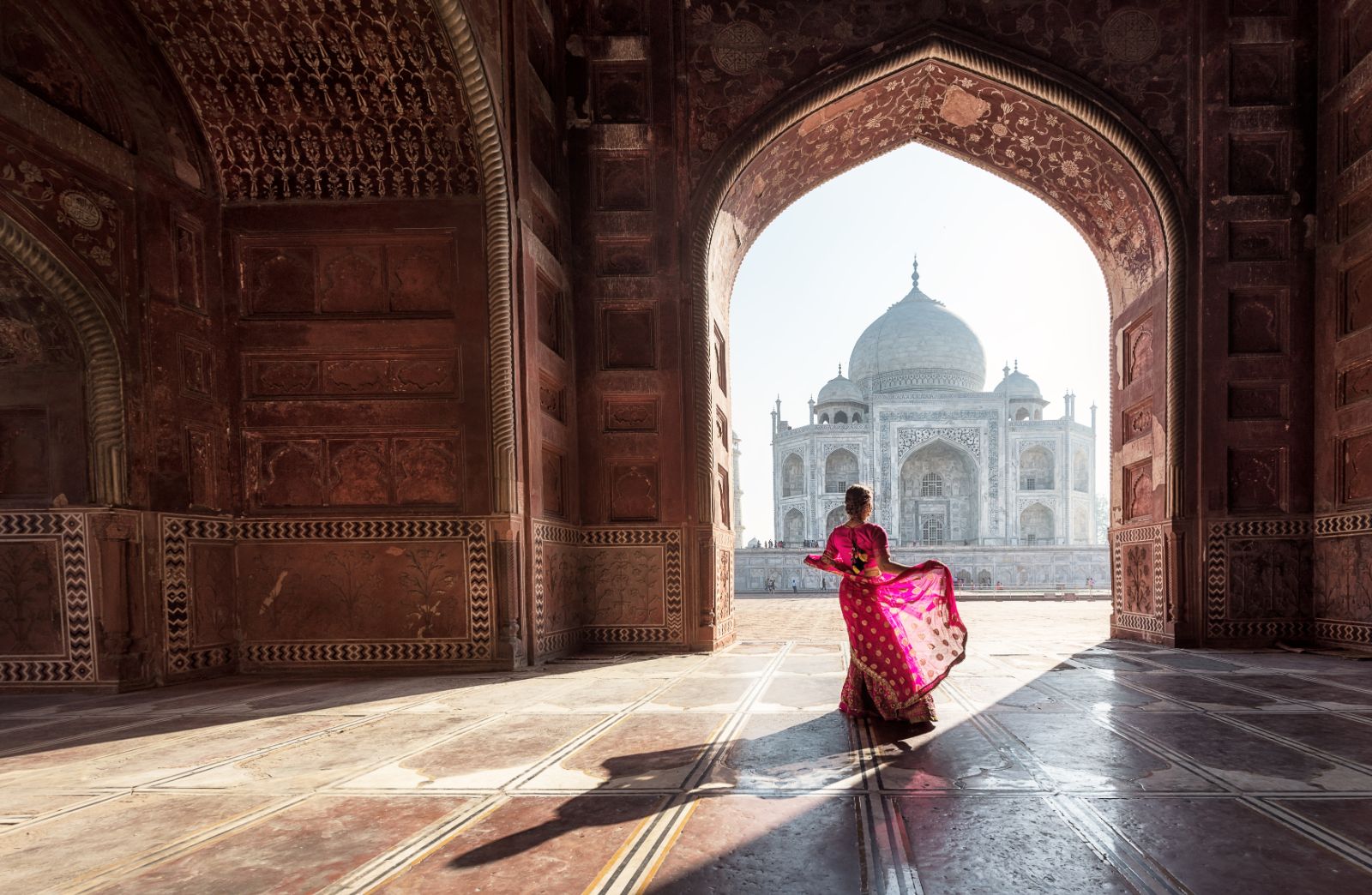 Woman in red sari dancing in the entrance archway to the Taj Mahal in Agra, Rajasthan