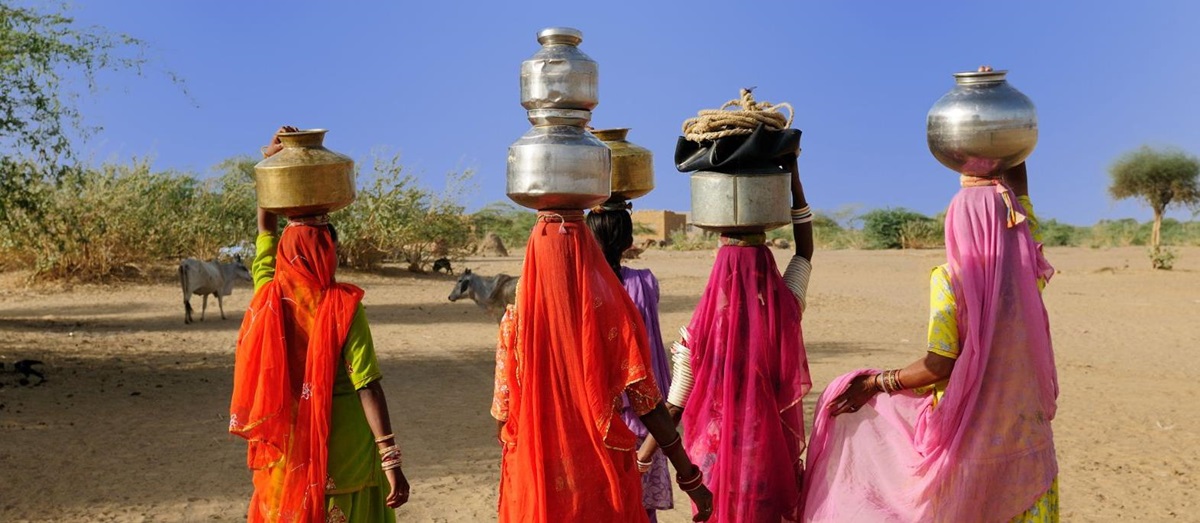 Women in colourful saris carrying pots on their heads in the Thar Desert, India