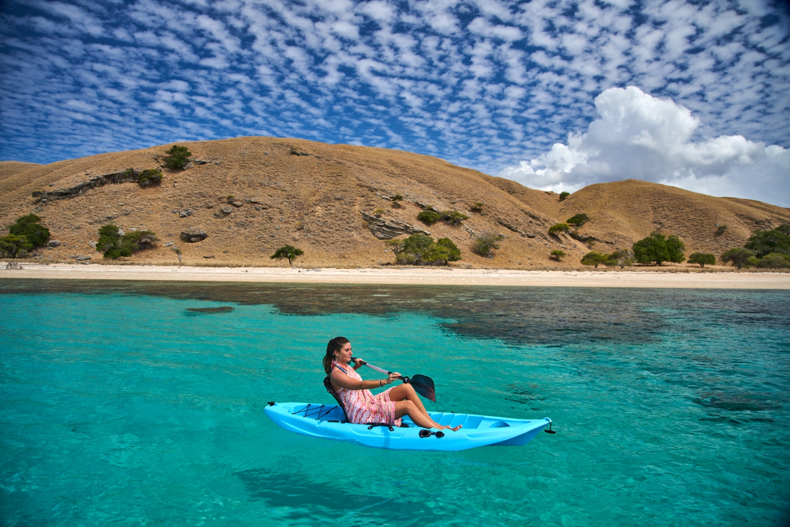 Woman on blue canoe floating near beach in Komodo