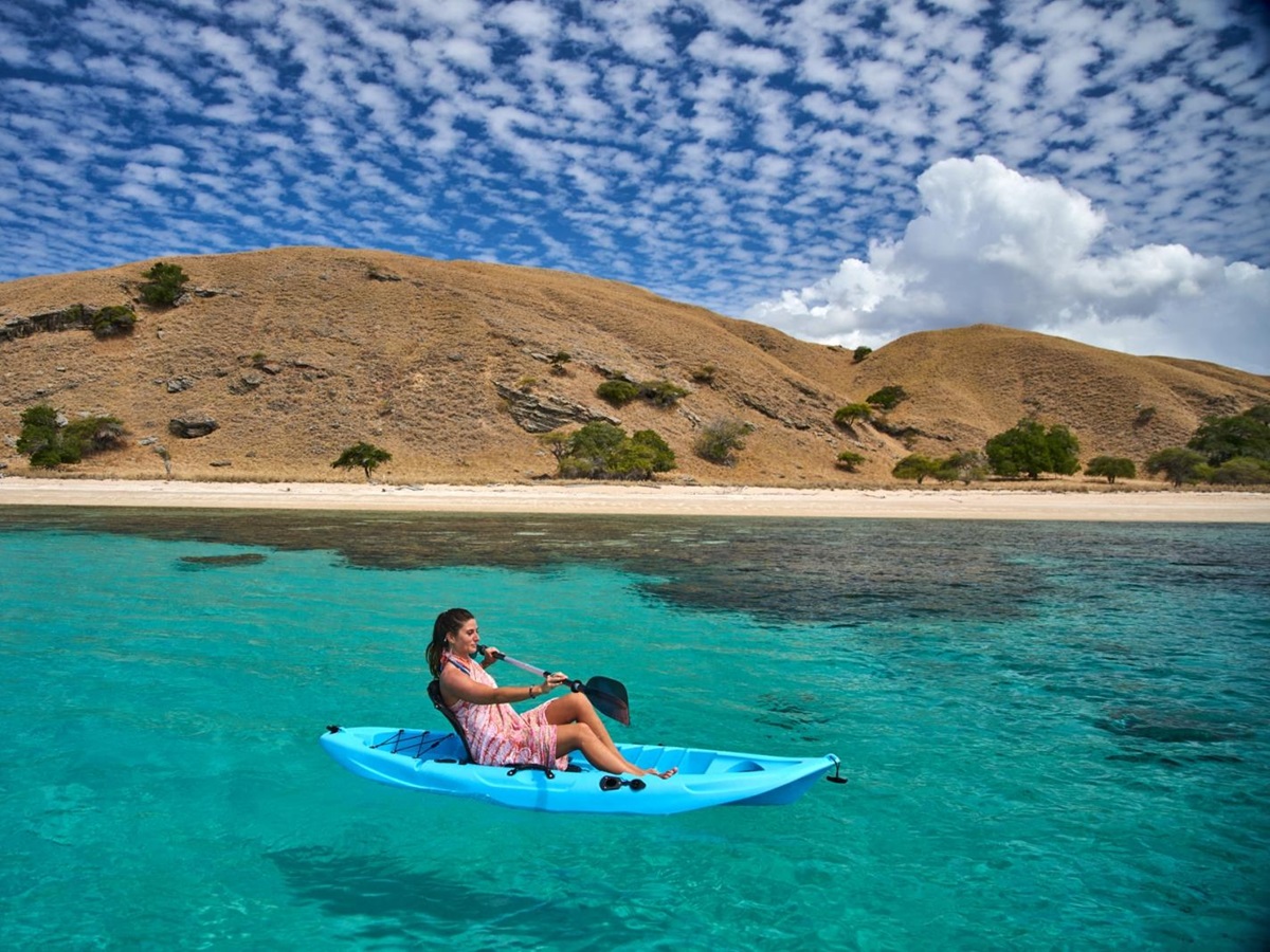 Woman on blue canoe floating near beach in Komodo