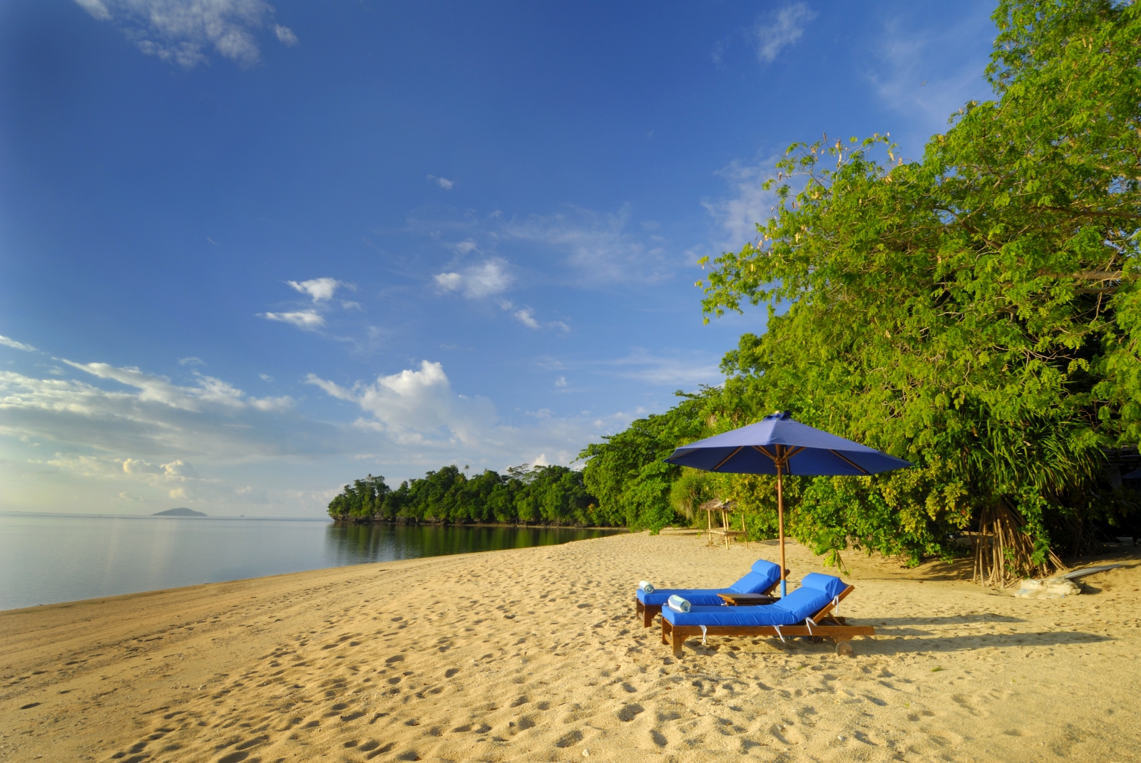 Two deck chairs on a sandy beach with a view out to sea at hotel Siladen in Indonesia