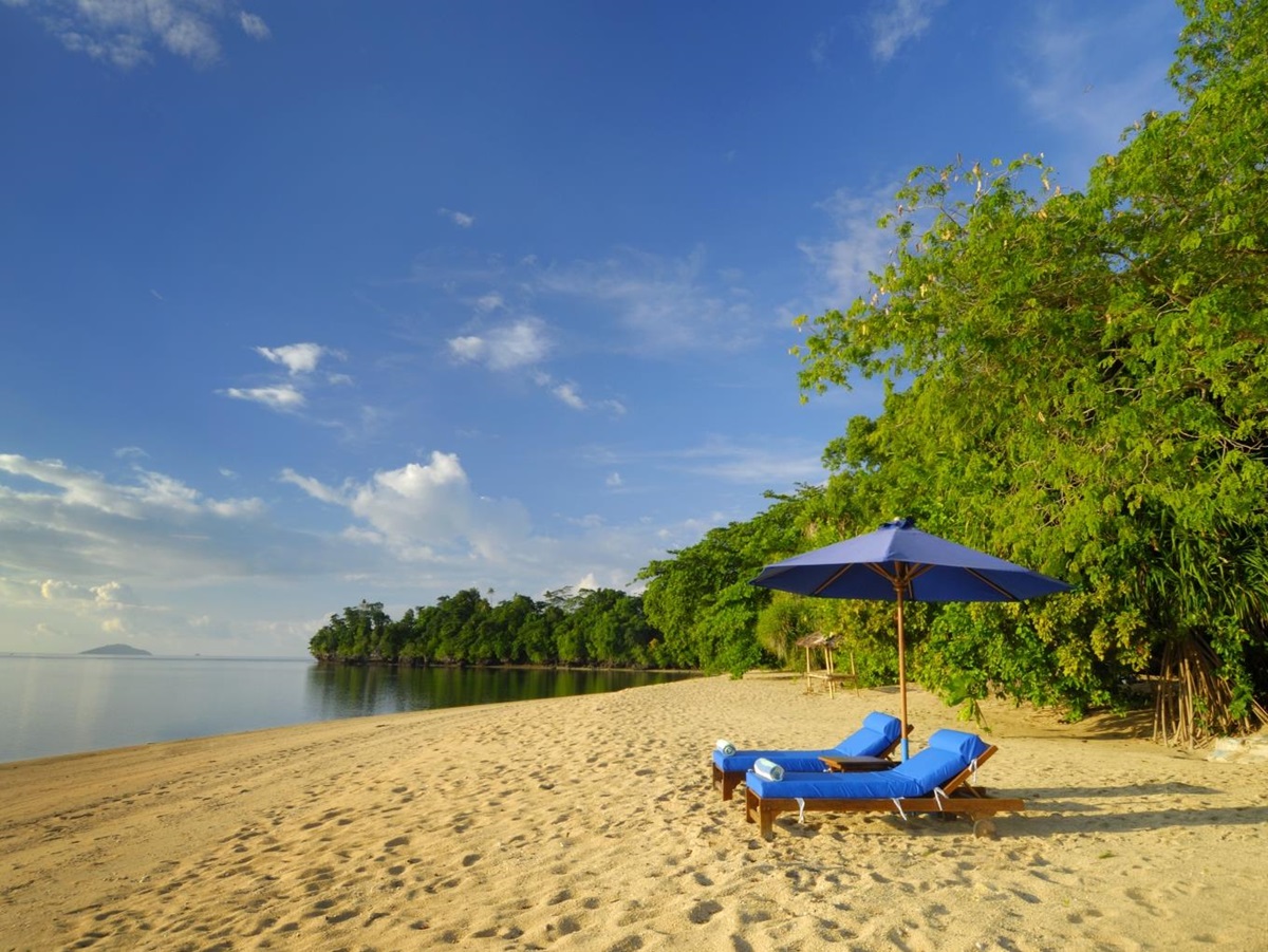 Two deck chairs on a sandy beach with a view out to sea at hotel Siladen in Indonesia