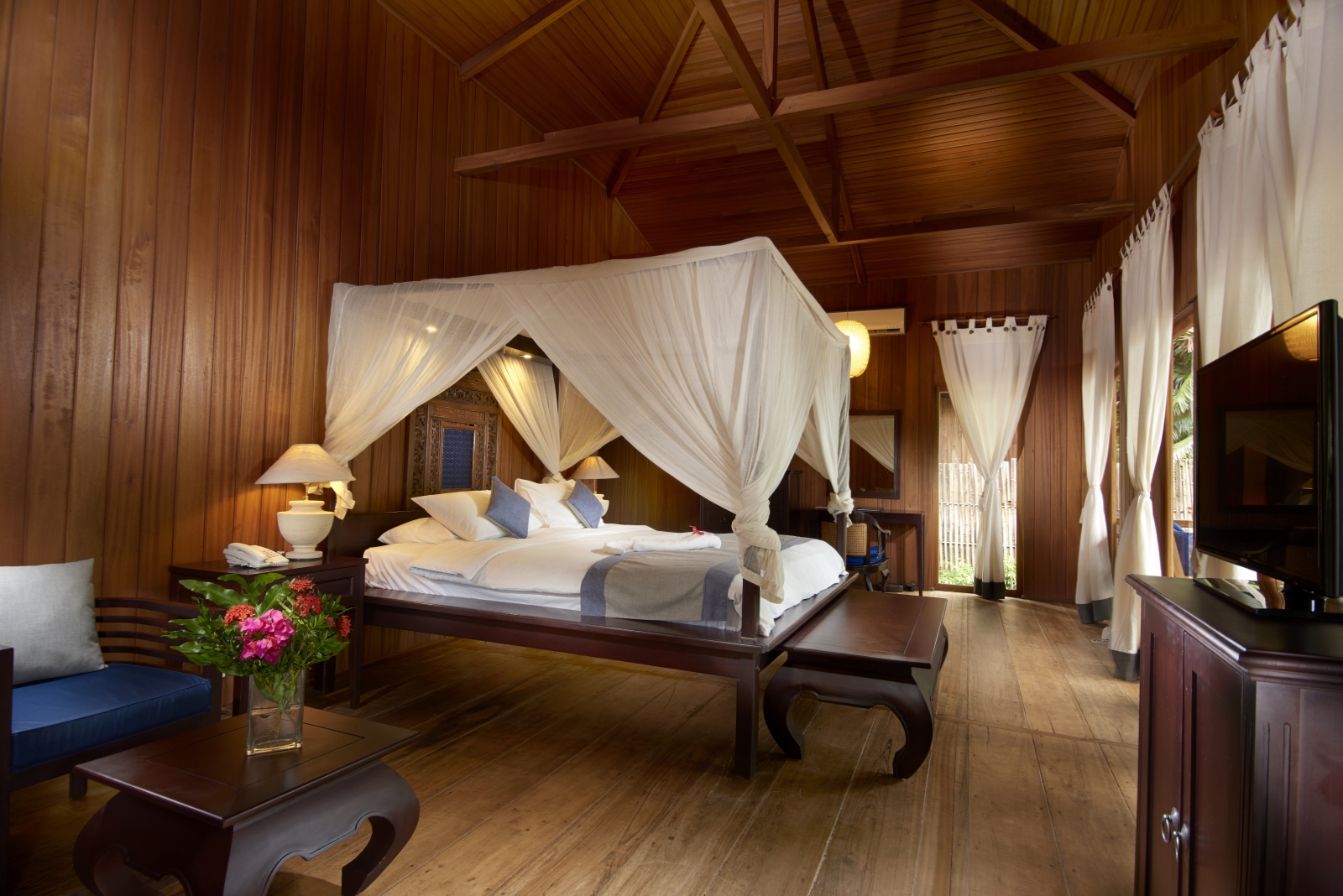 King bed in a large wooden room with white drapes and curtains at hotel Siladen in Indonesia