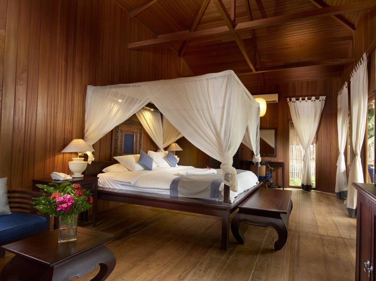 King bed in a large wooden room with white drapes and curtains at hotel Siladen in Indonesia