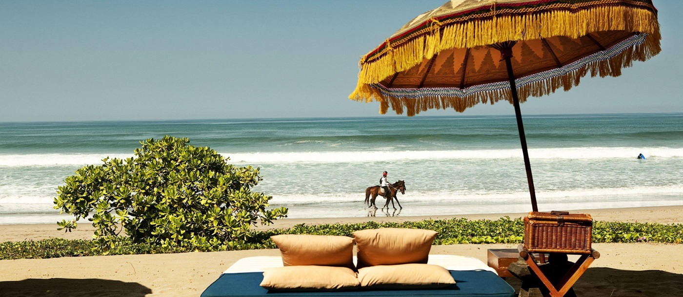 Day bed with horse rider in background at Oberoi Bali, Indonesia