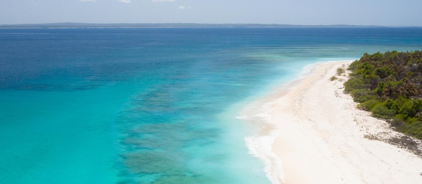 Aerial view of a couple walking along a deserted white sand beach 