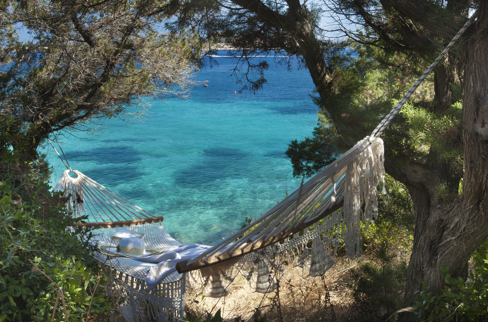 A hammock hidden between trees overlooking the turquoise waters of the Mediterranean at luxury hotel Capo d'Orso on Sardinia, Italy