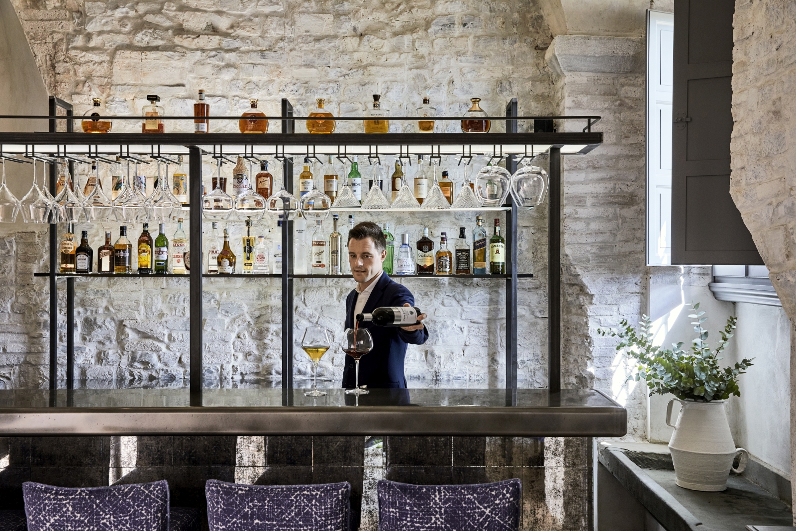 Bar tender serving drinks at the bar of La Taverna at luxury resort COMO Castello del Nero in Italy