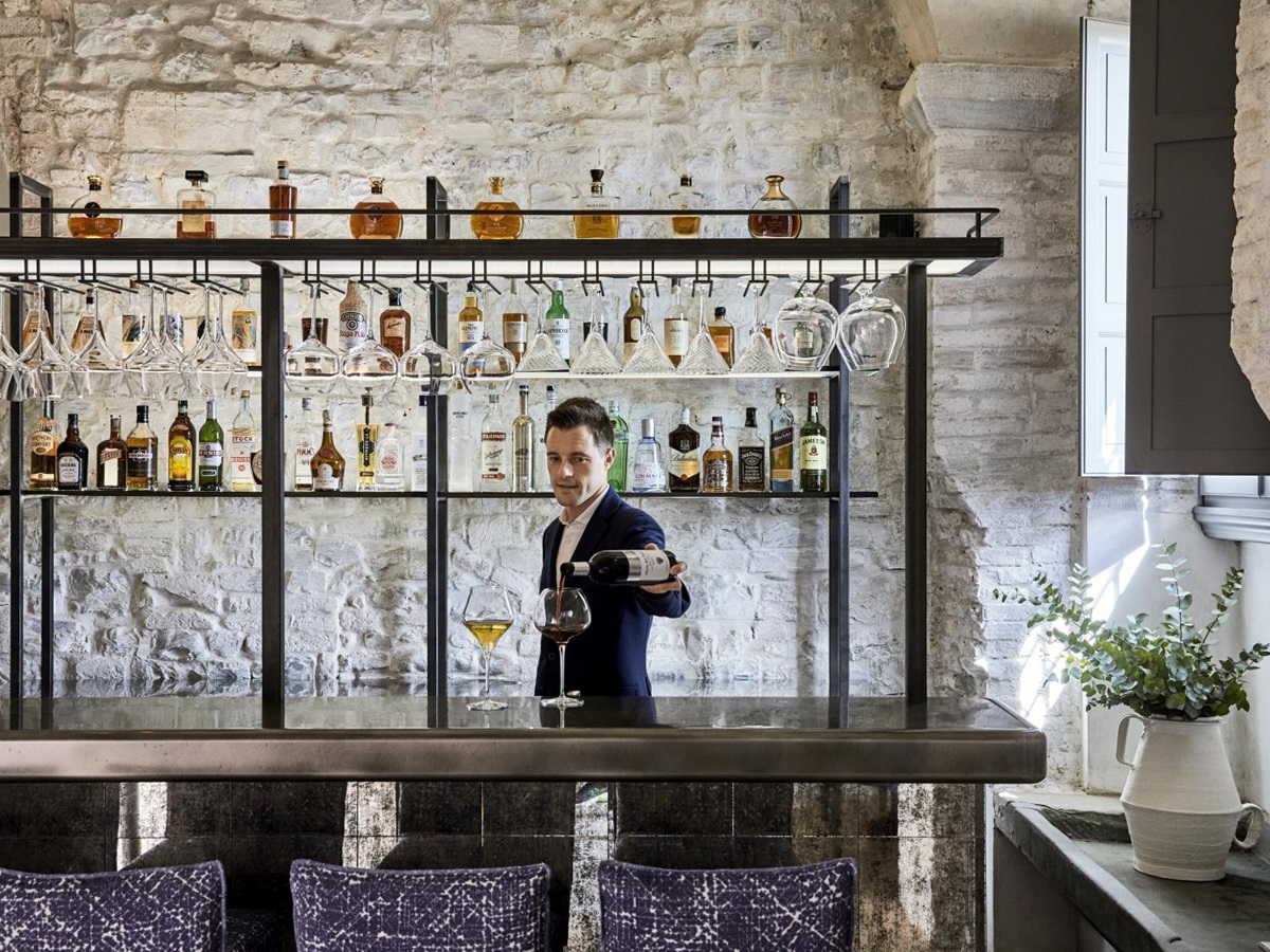 Bar tender serving drinks at the bar of La Taverna at luxury resort COMO Castello del Nero in Italy
