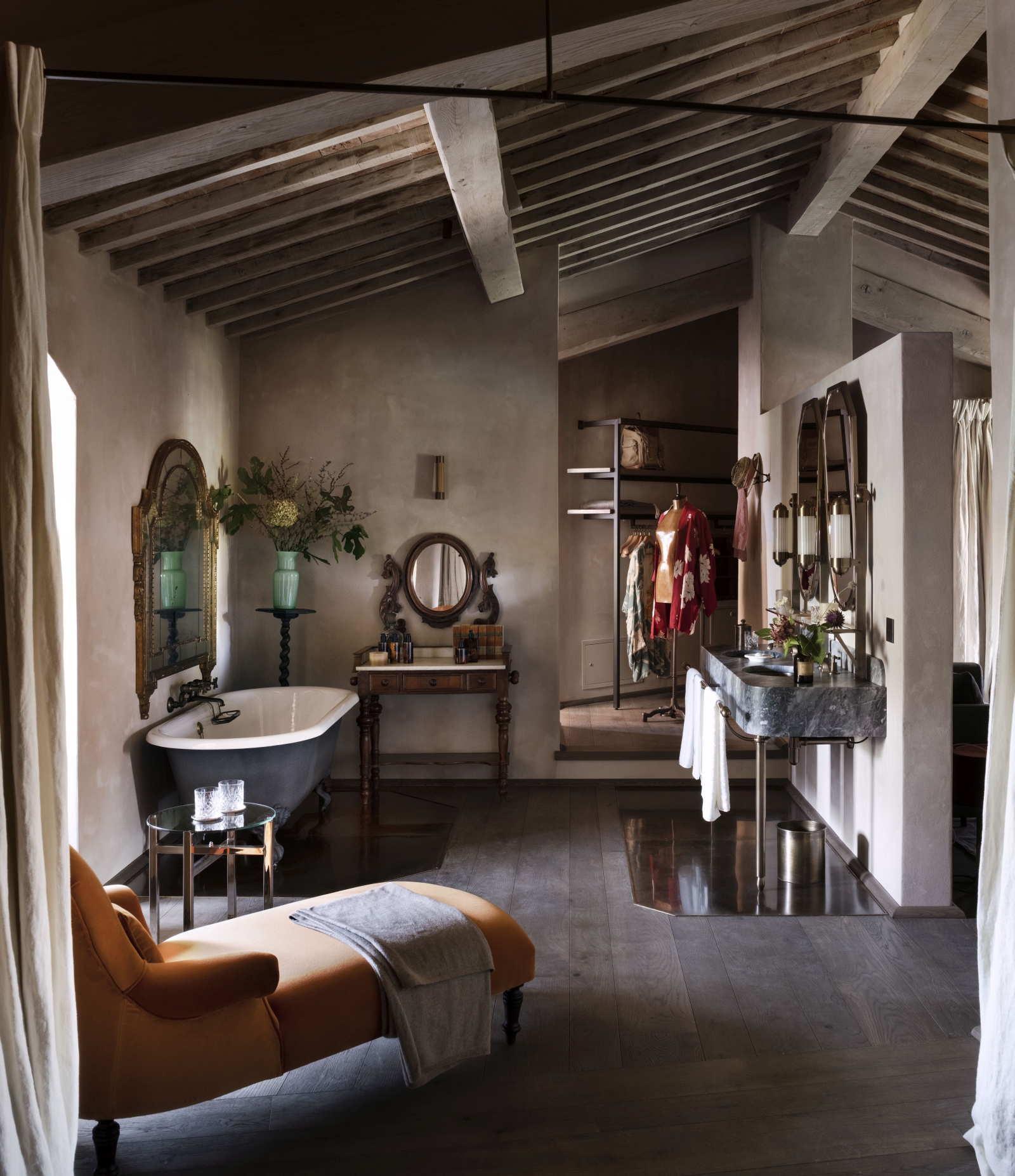 Spacious en-suite bathroom with antique bathtub, marble sinks, a chaise lounge and walk-in closet at luxury hotel Castello di Reschio in Umbria, Italy
