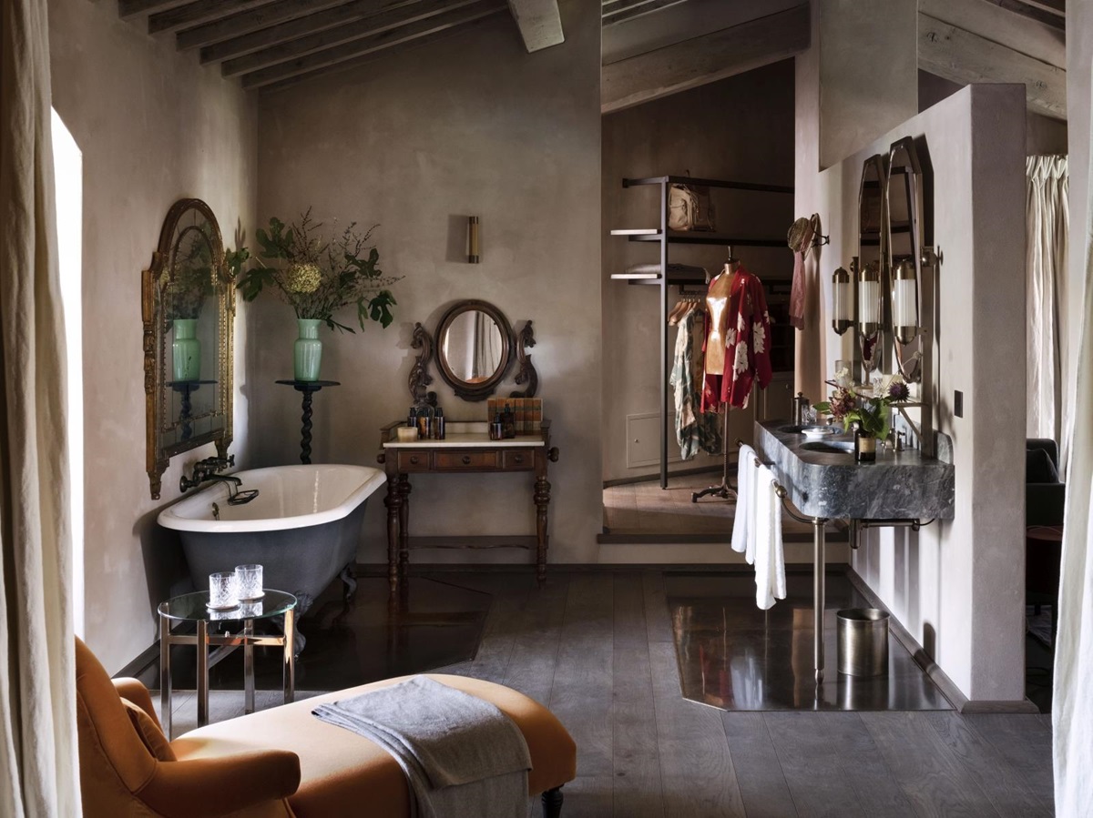 Spacious en-suite bathroom with antique bathtub, marble sinks, a chaise lounge and walk-in closet at luxury hotel Castello di Reschio in Umbria, Italy