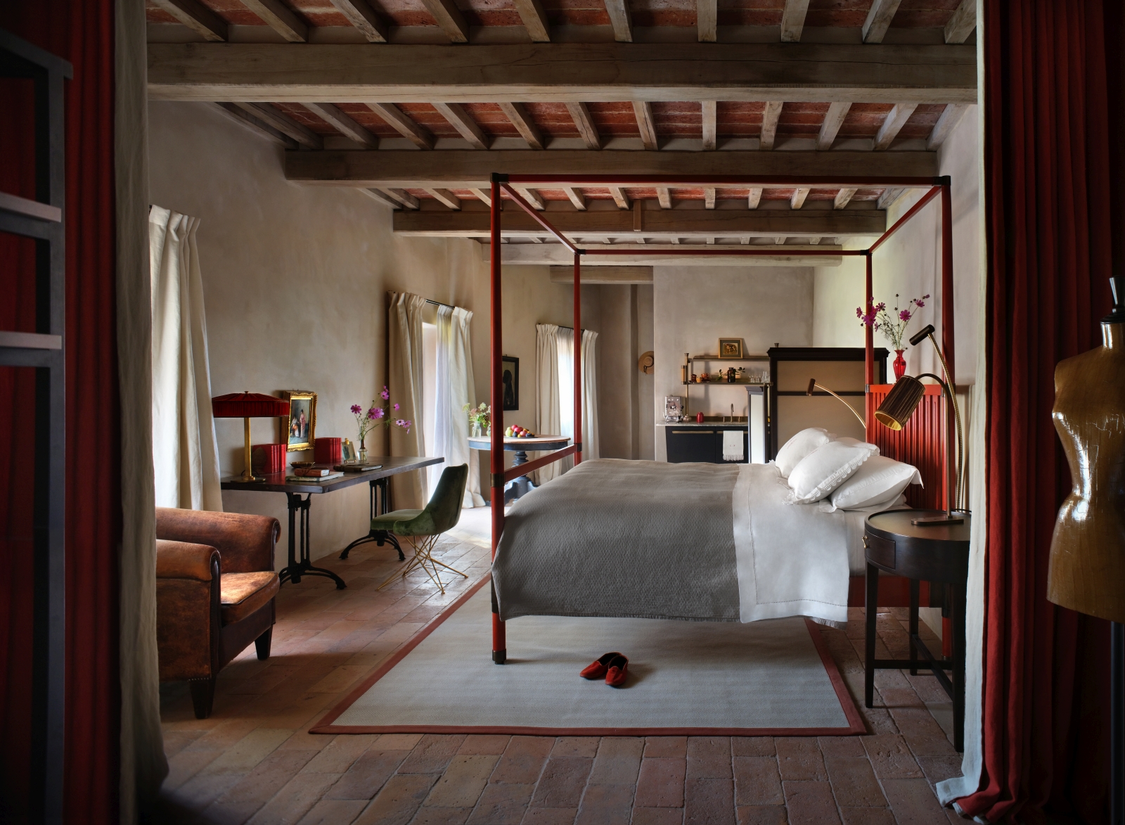 Rustic bedroom at luxury hotel Castello di Reschio in Umbria, Italy with four poster bed, desk, a walk-in closet and three large floor-to-ceiling windows
