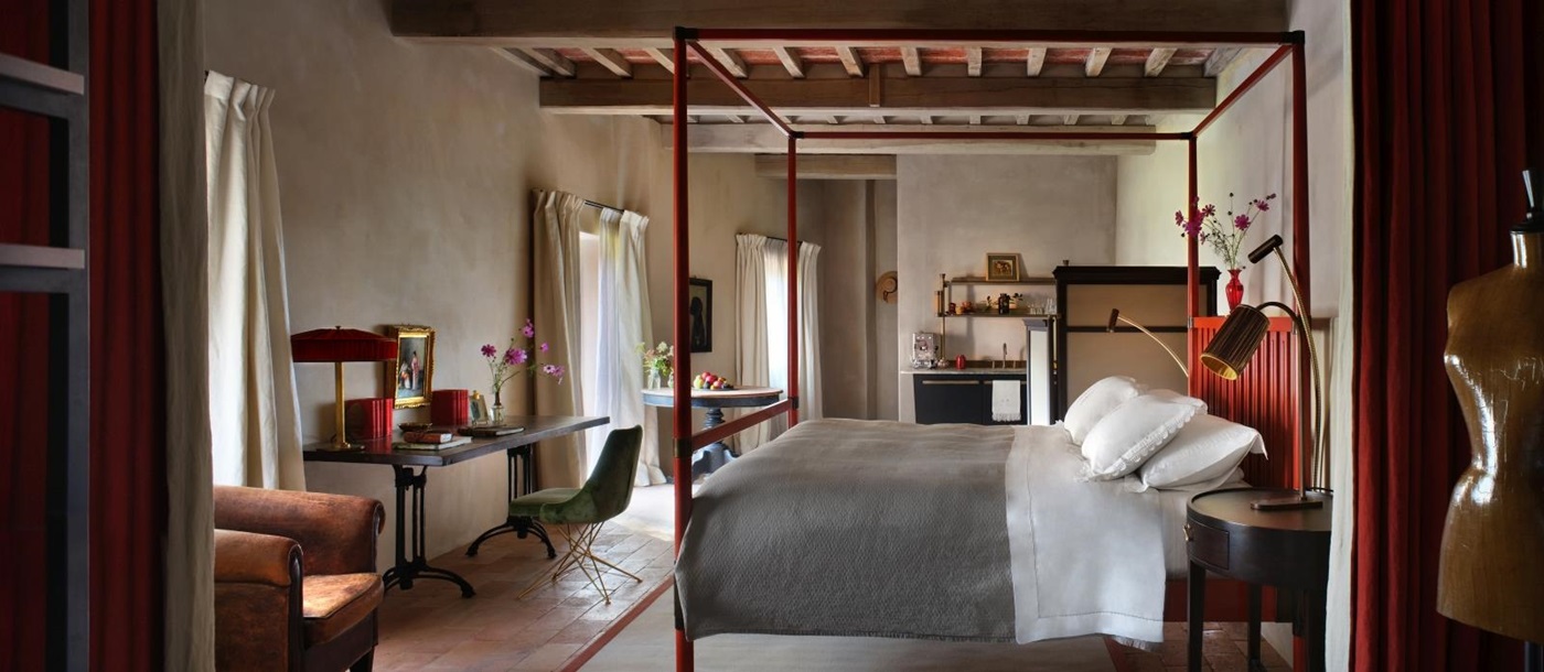 Rustic bedroom at luxury hotel Castello di Reschio in Umbria, Italy with four poster bed, desk, a walk-in closet and three large floor-to-ceiling windows