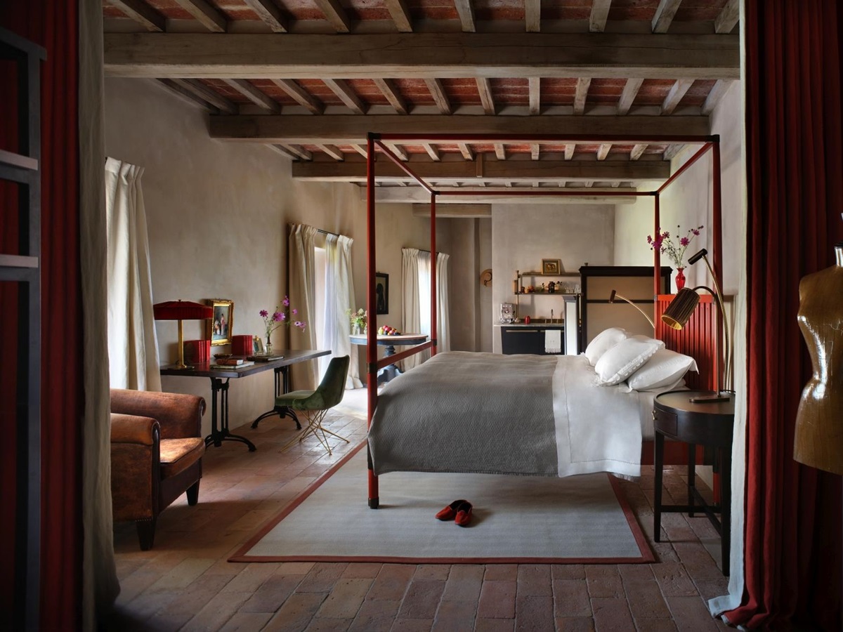 Rustic bedroom at luxury hotel Castello di Reschio in Umbria, Italy with four poster bed, desk, a walk-in closet and three large floor-to-ceiling windows