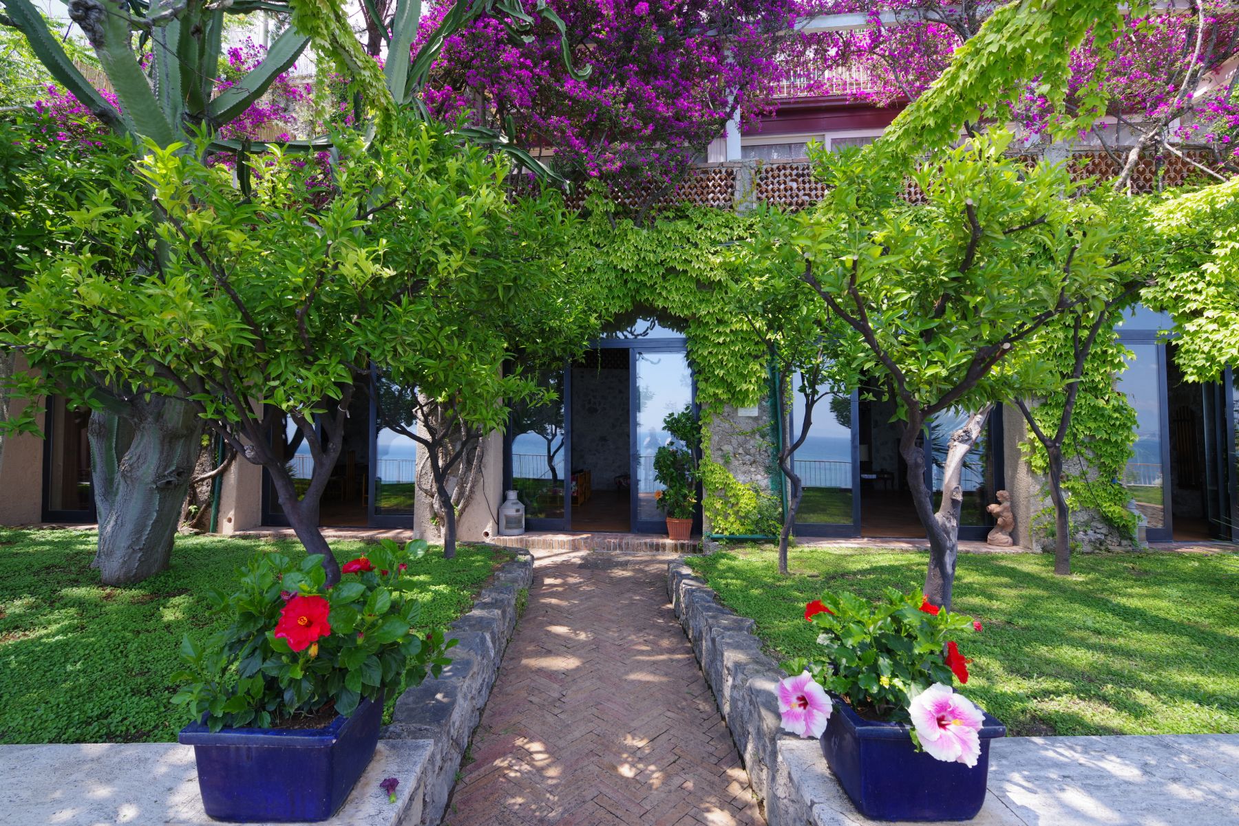 View of the main entrance with flowers and trees and large glass doors at Castello Sul Mare in Amalfi