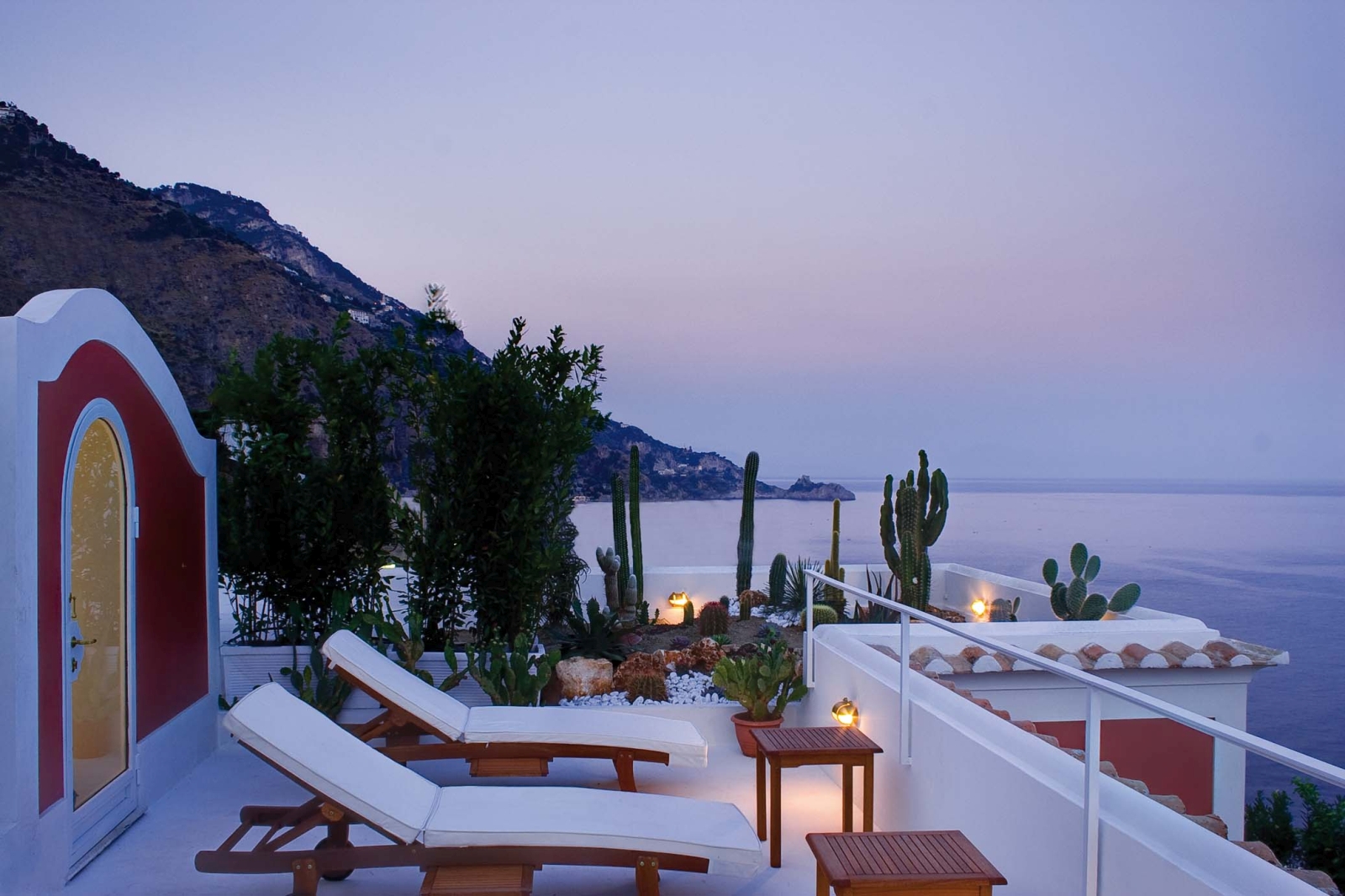 Balcony at sunset with sun loungers, coffee tables, cacti, and sea view at Villa di Praiano on the Amalfi Coast in Italy
