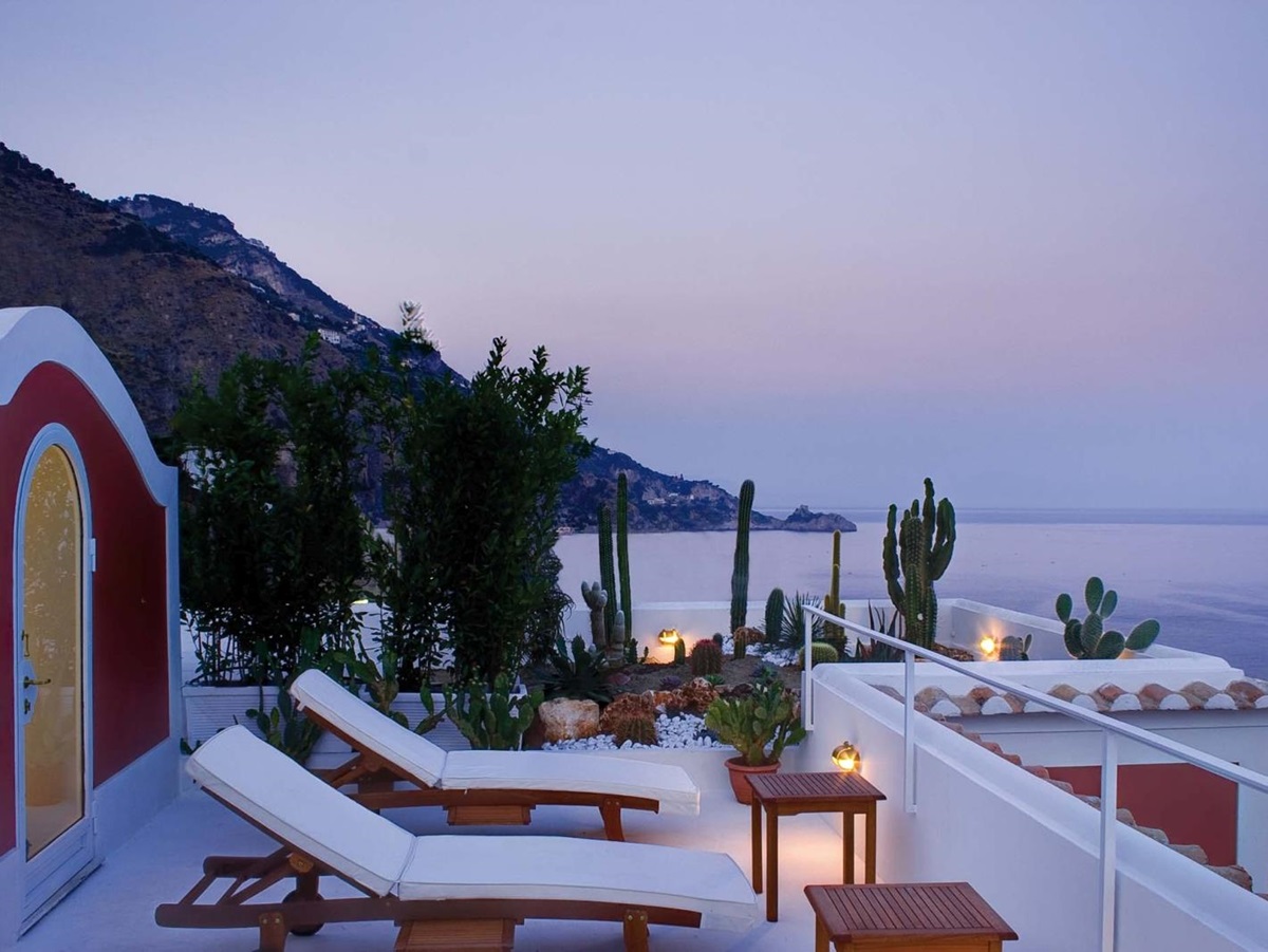 Balcony at sunset with sun loungers, coffee tables, cacti, and sea view at Villa di Praiano on the Amalfi Coast in Italy