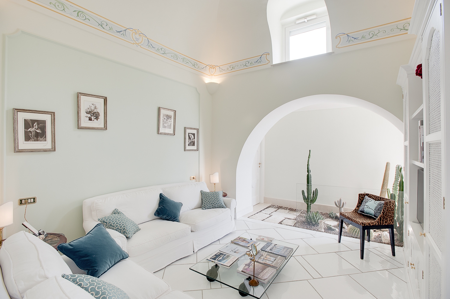 Living room with white sofas, table, picture frames, armchair and cacti at Villa di Praiano on the Amalfi Coast in Italy