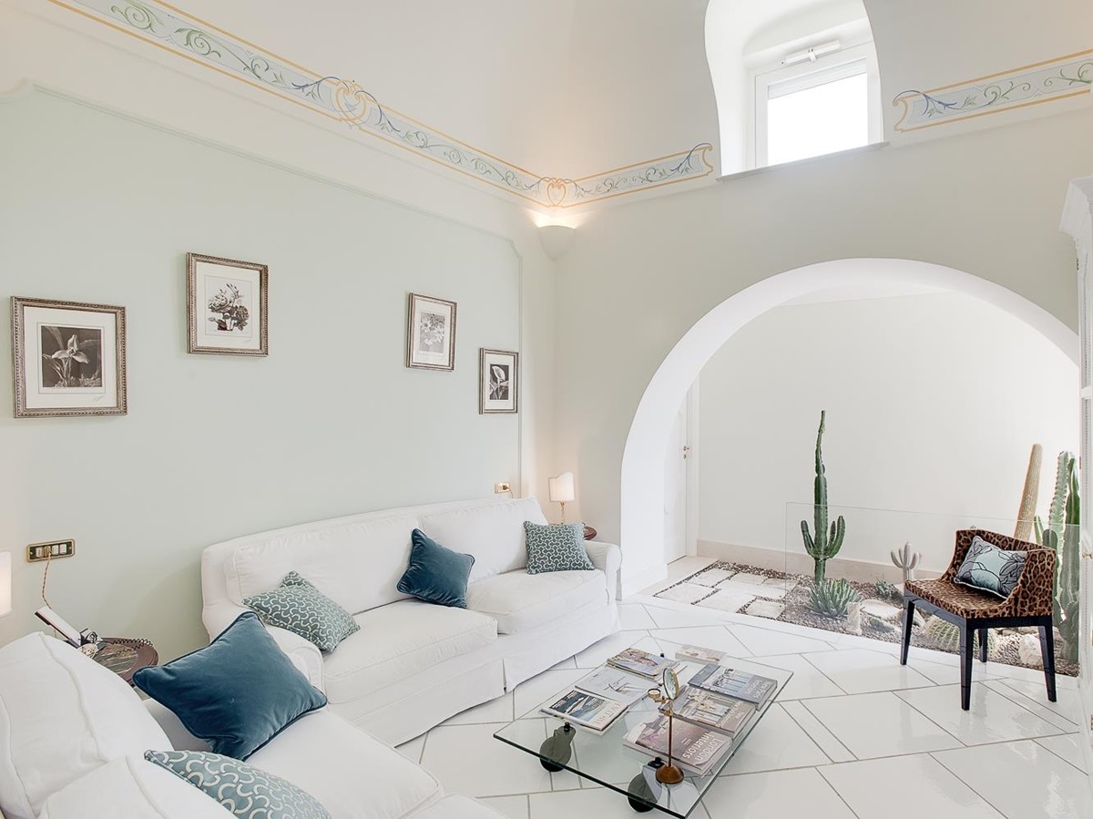 Living room with white sofas, table, picture frames, armchair and cacti at Villa di Praiano on the Amalfi Coast in Italy