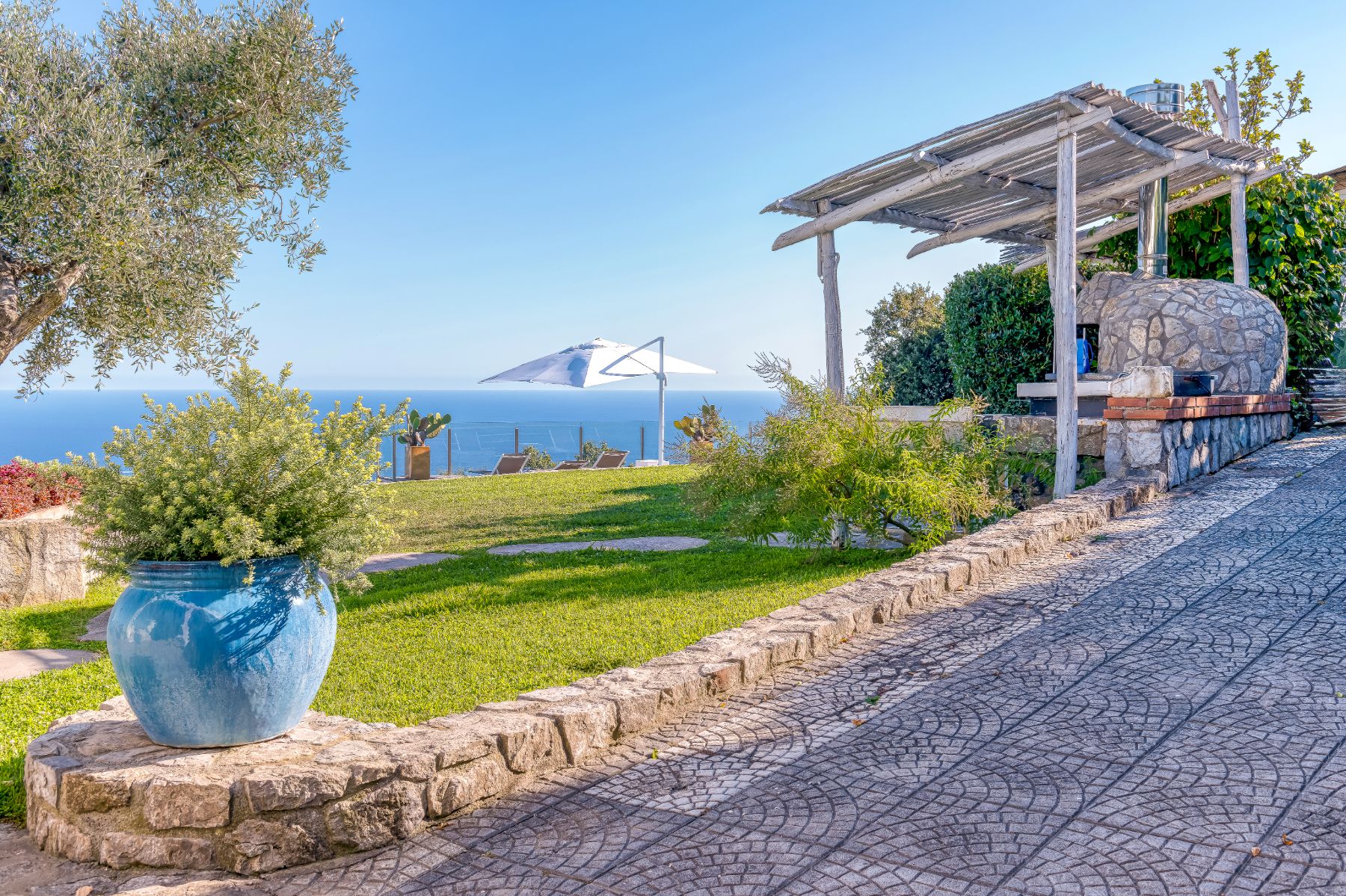 View from the patio of the grass area, with the pool terrace and sea view in the background at Villa Li Galli in Amalfi