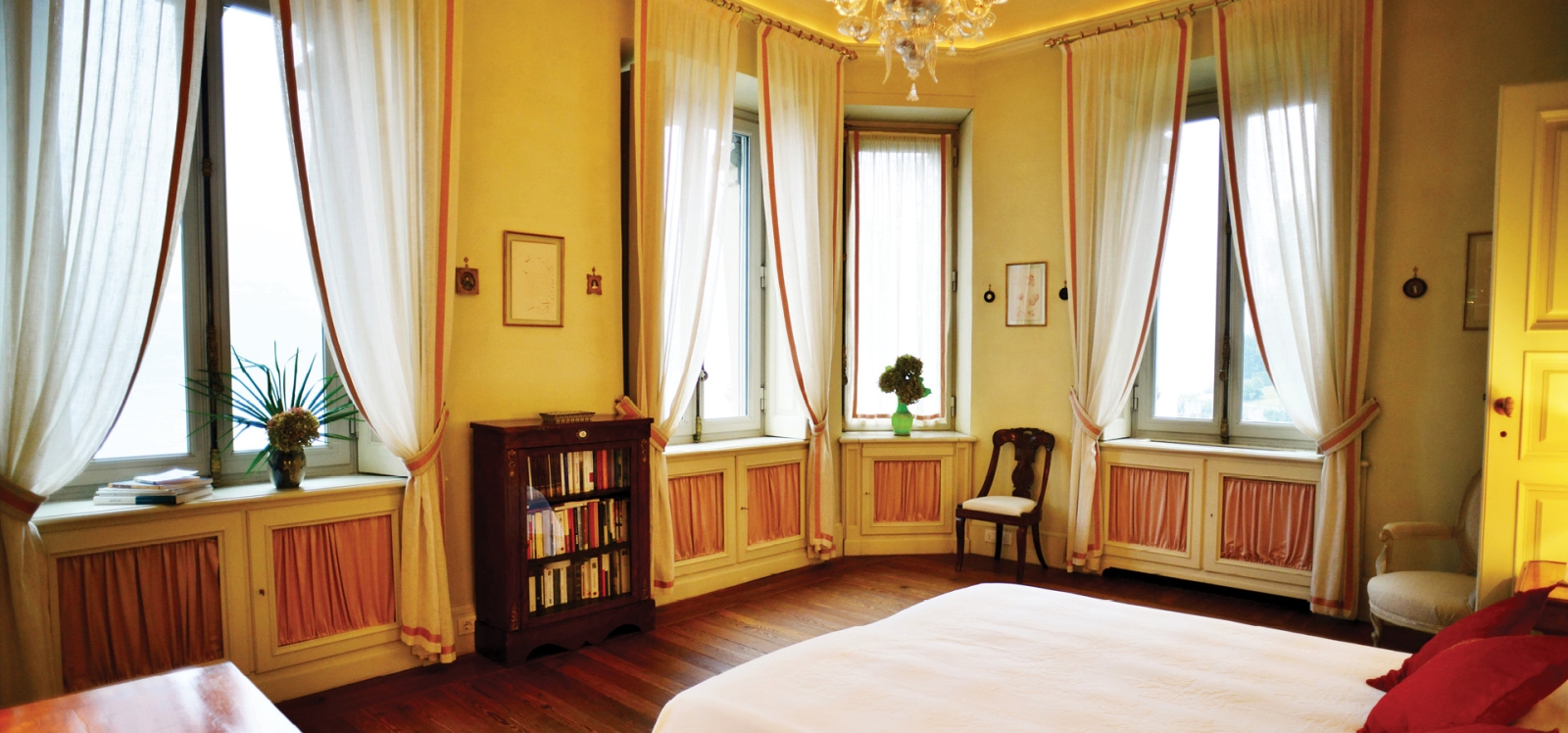 Bedroom with double bed, windows, bookshelf and chandelier at Ville del Lago on Lake Como, Italy
