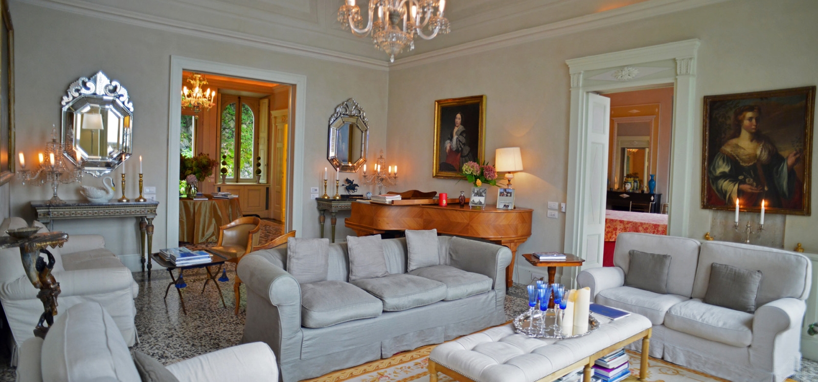 Living room with sofas, grand piano, portraits, mirrors and chandelier at Ville del Lago on Lake Como, Italy