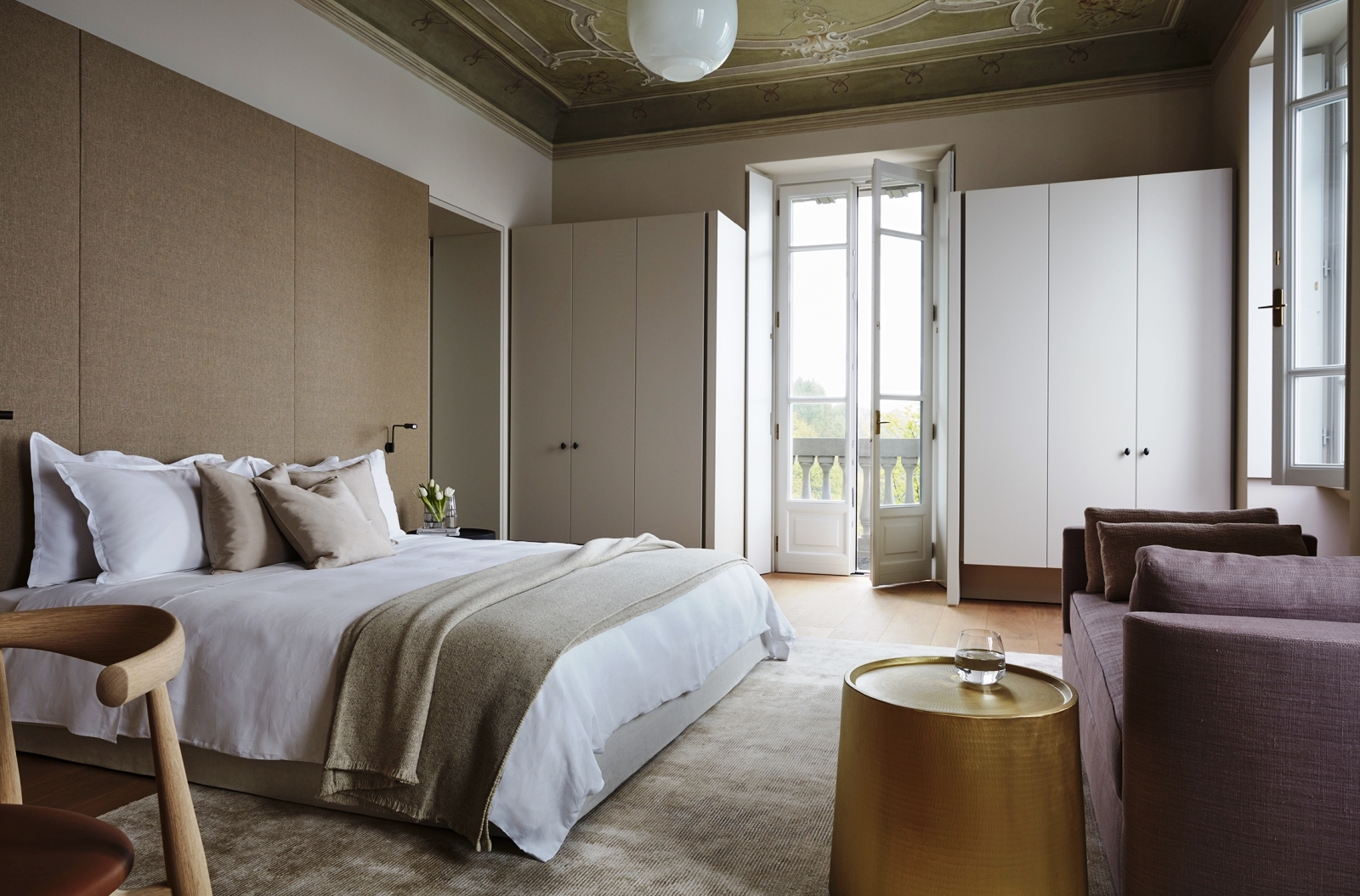 Double bedroom with chair, purple sofa, golden table, wardrobes and french doors at Villa della Vetta on Lake Como in Italy