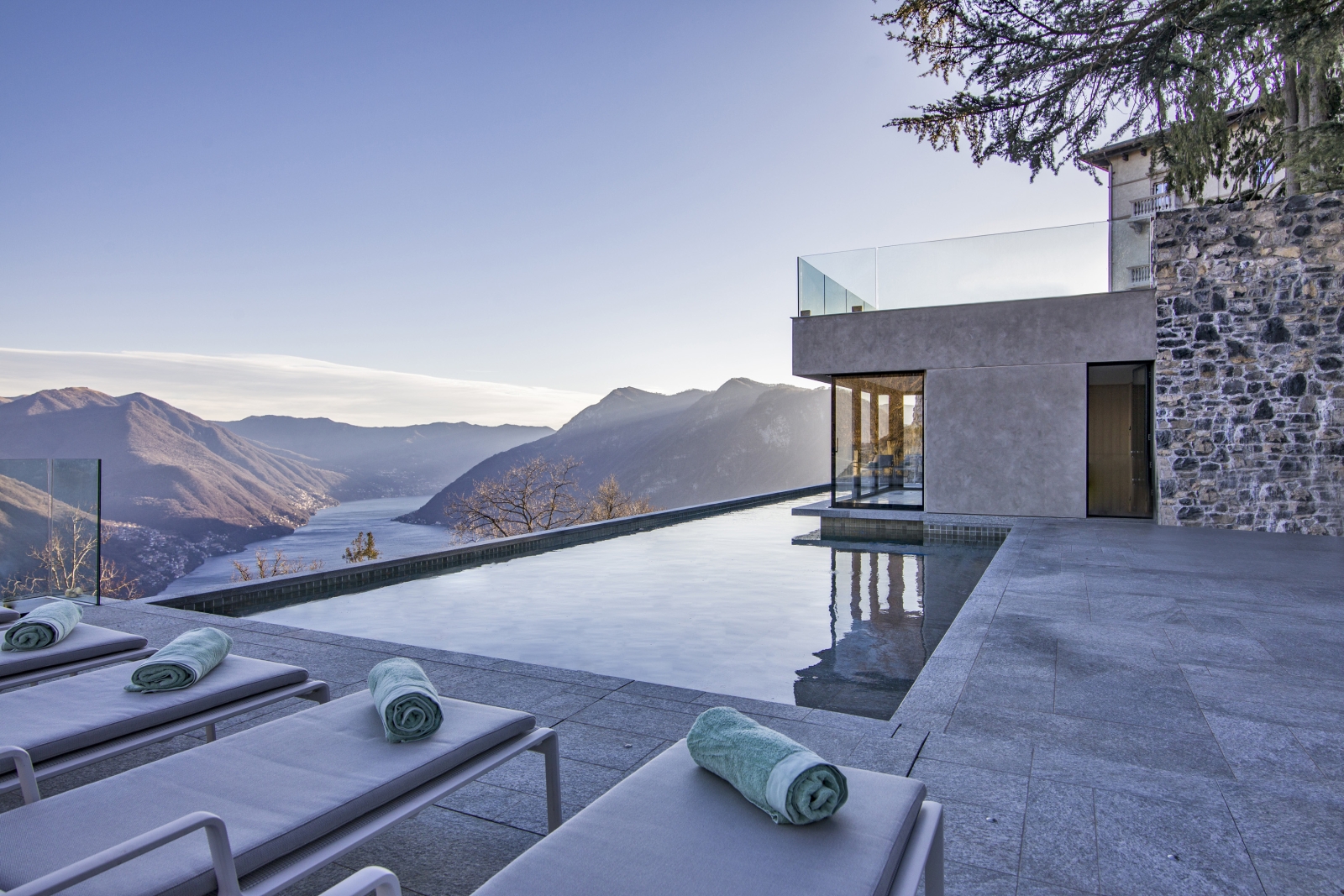 Pool area with four sun loungers and blue towels and view of Lake Como at Villa della Vetta on Lake Como in Italy