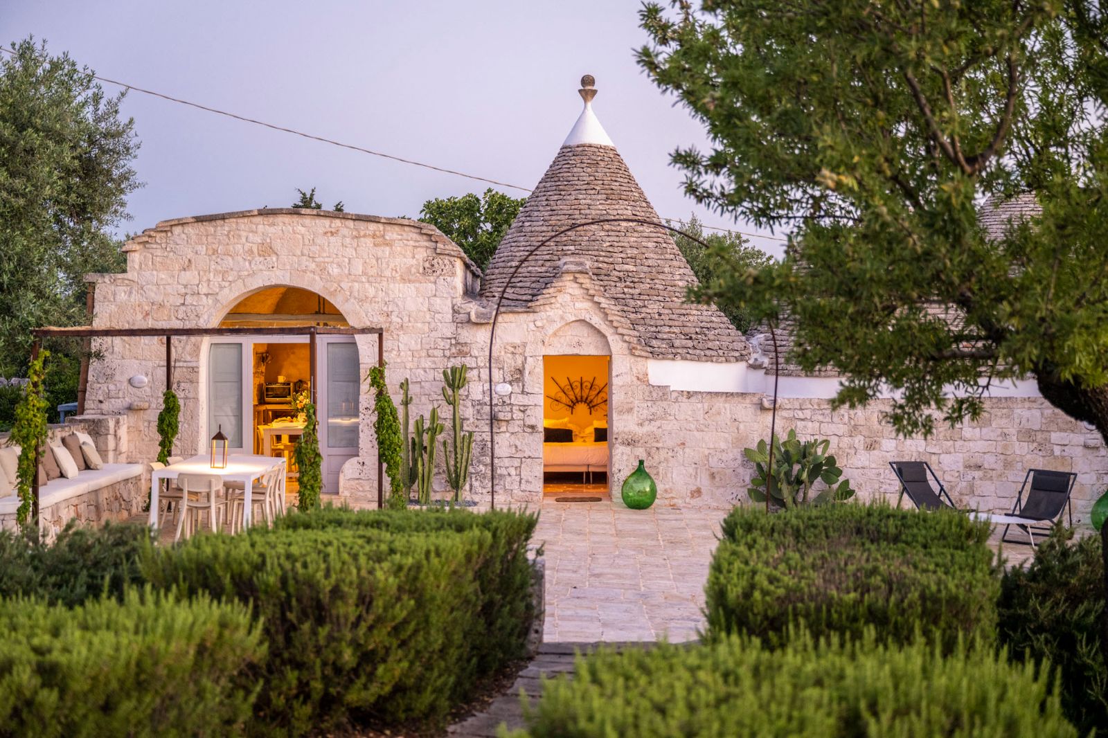 Exterior view of villa and patio with sun loungers, dining tables and chairs at Masseria Bianco in Puglia, Italy