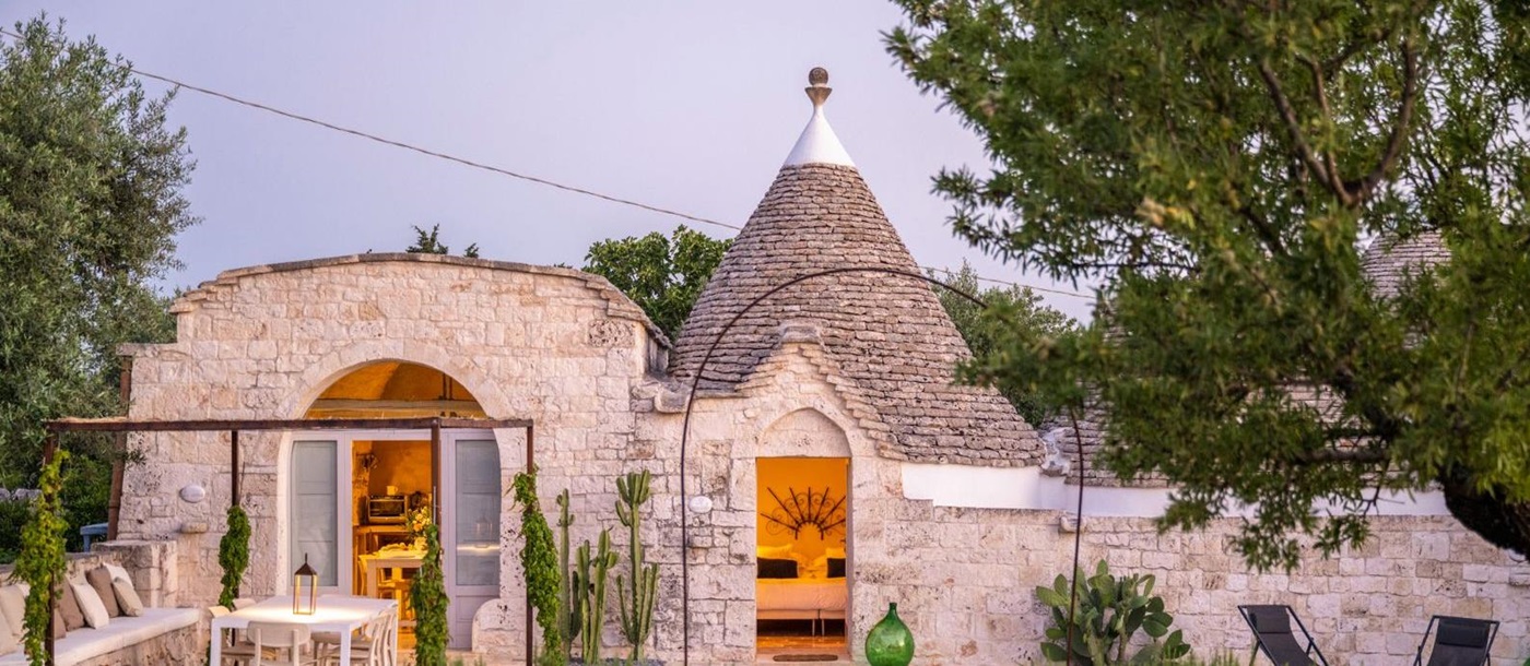 Exterior view of villa and patio with sun loungers, dining tables and chairs at Masseria Bianco in Puglia, Italy