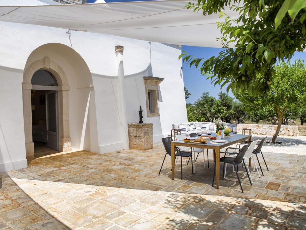 Outdoor dining area with dining table, chairs, sofa, water fountain and trees at Masseria Bianco in Puglia, Italy