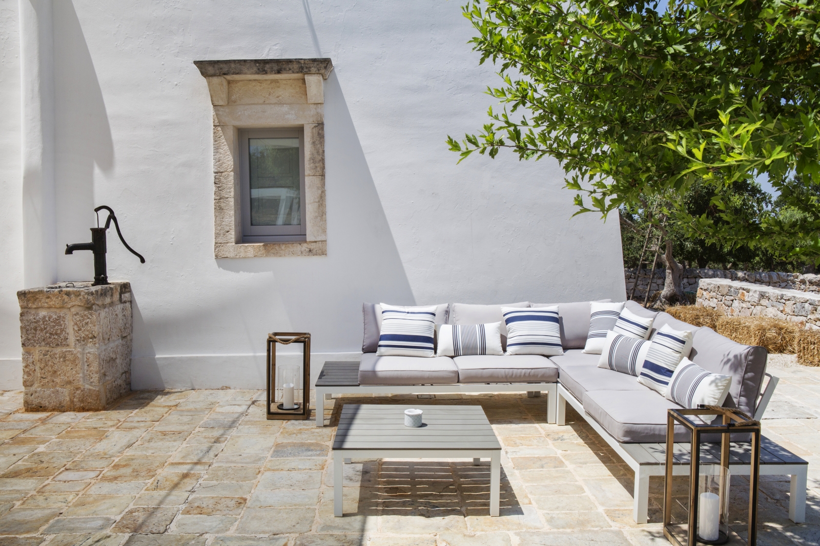 Outdoor lounge area with sofa, cushions, coffee table, lanterns, water fountain and tree at Masseria Bianco in Puglia, Italy