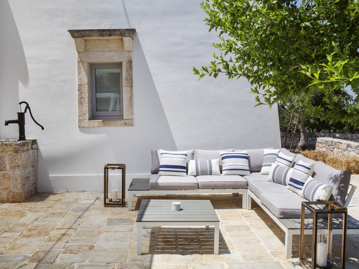 Outdoor lounge area with sofa, cushions, coffee table, lanterns, water fountain and tree at Masseria Bianco in Puglia, Italy