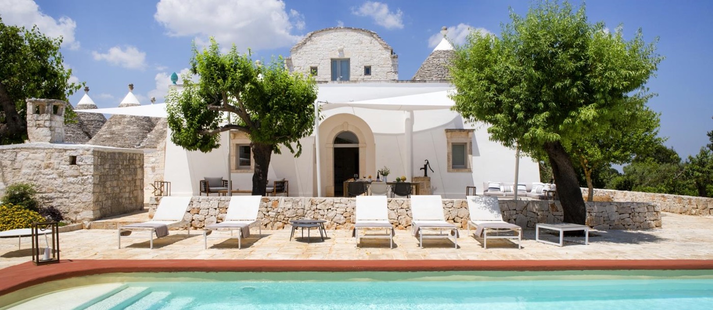 Pool and pool area with sun loungers, coffee table and trees at Masseria Bianco in Puglia, Italy