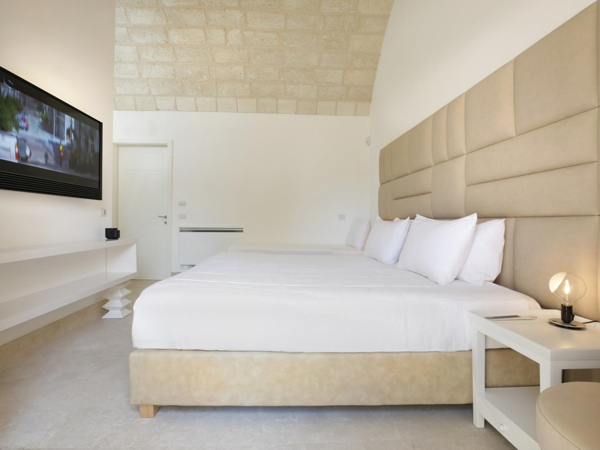 Bedroom with double bed, single bed, bedside table, lamp, TV and stone ceiling at Masseria dei Papi in Puglia, Italy