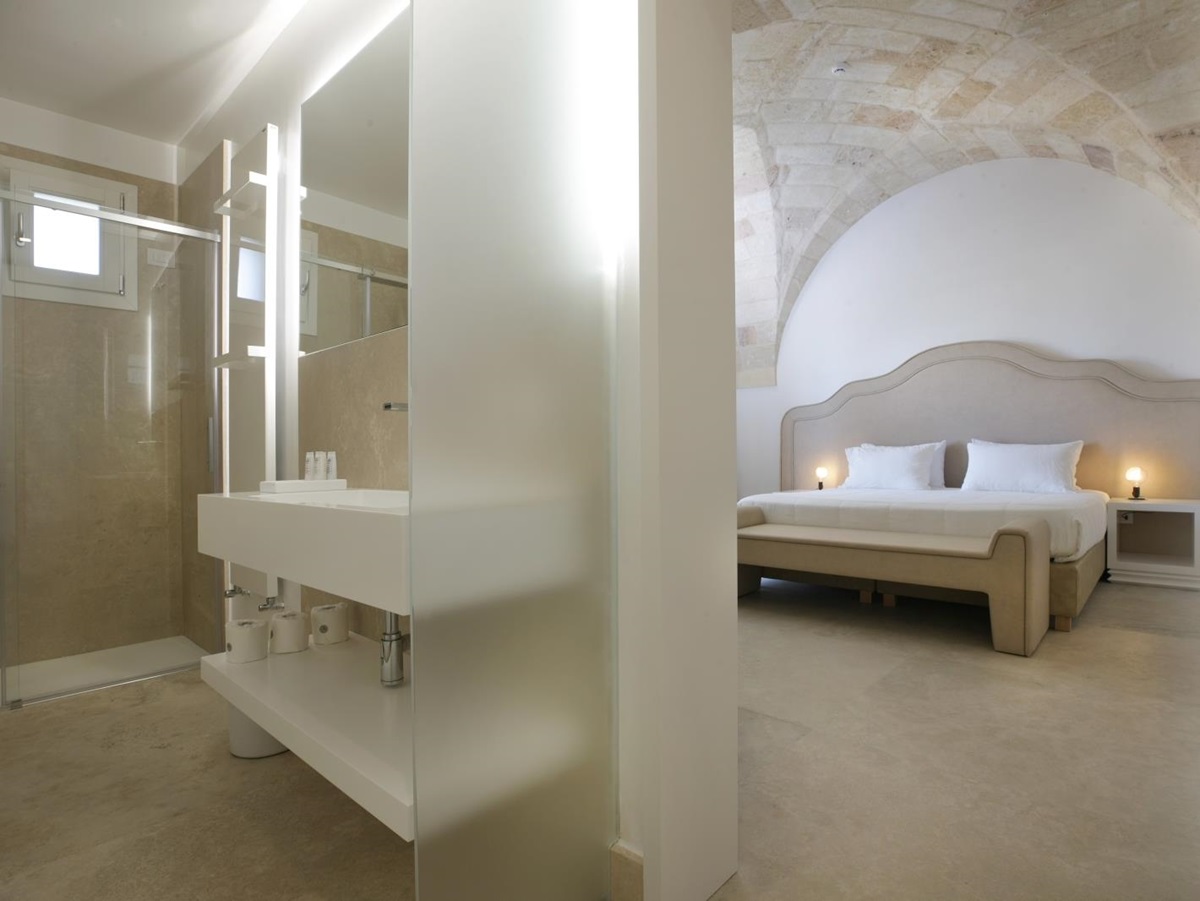Bedroom with double bed, bedside table, lamp and ensuite with sink, shower and mirror at Masseria dei Papi in Puglia, Italy