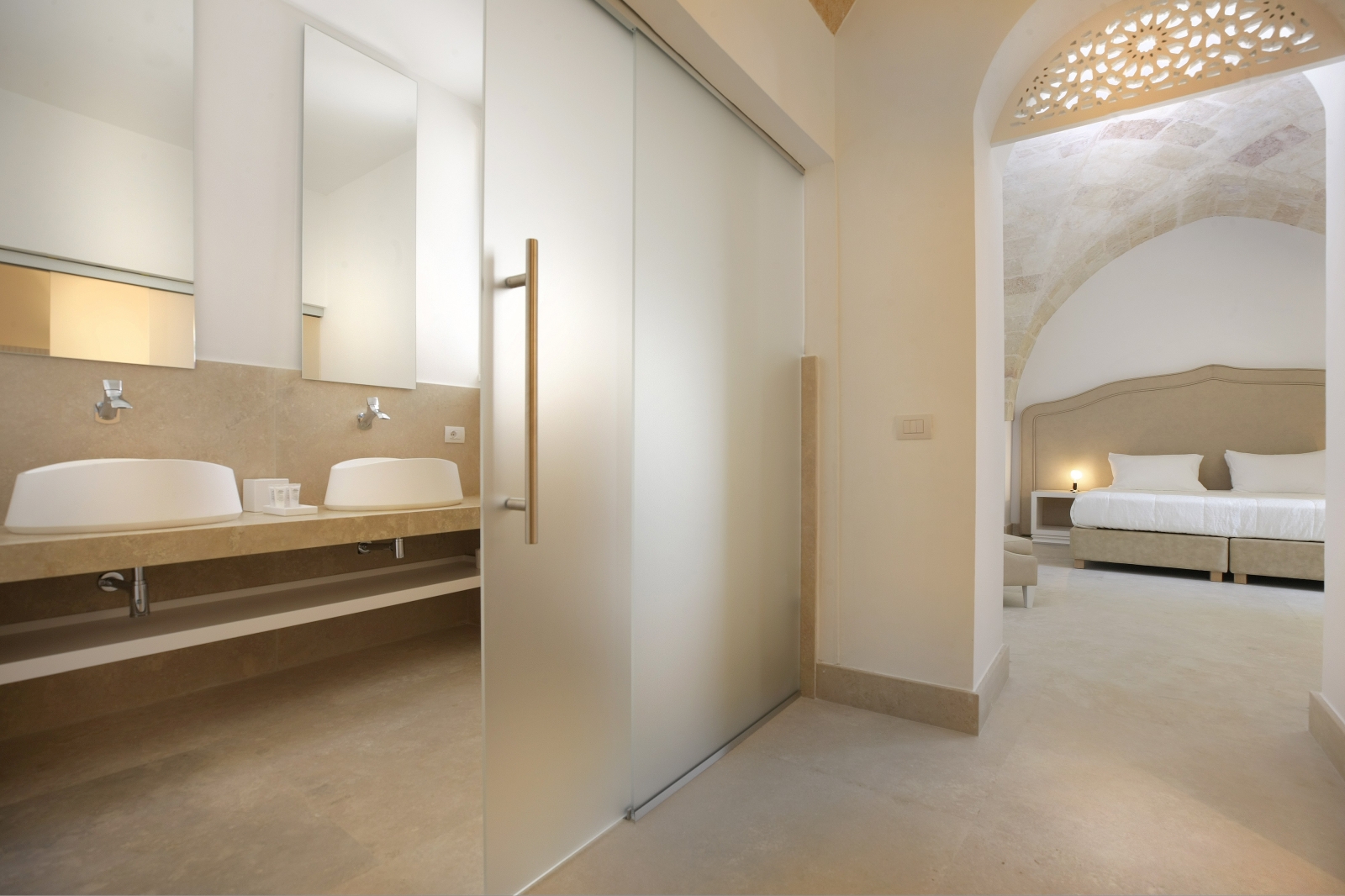 Bedroom with double bed, bedside table, lamp & ensuite bathroom with sinks and mirrors at Masseria dei Papi in Puglia, Italy