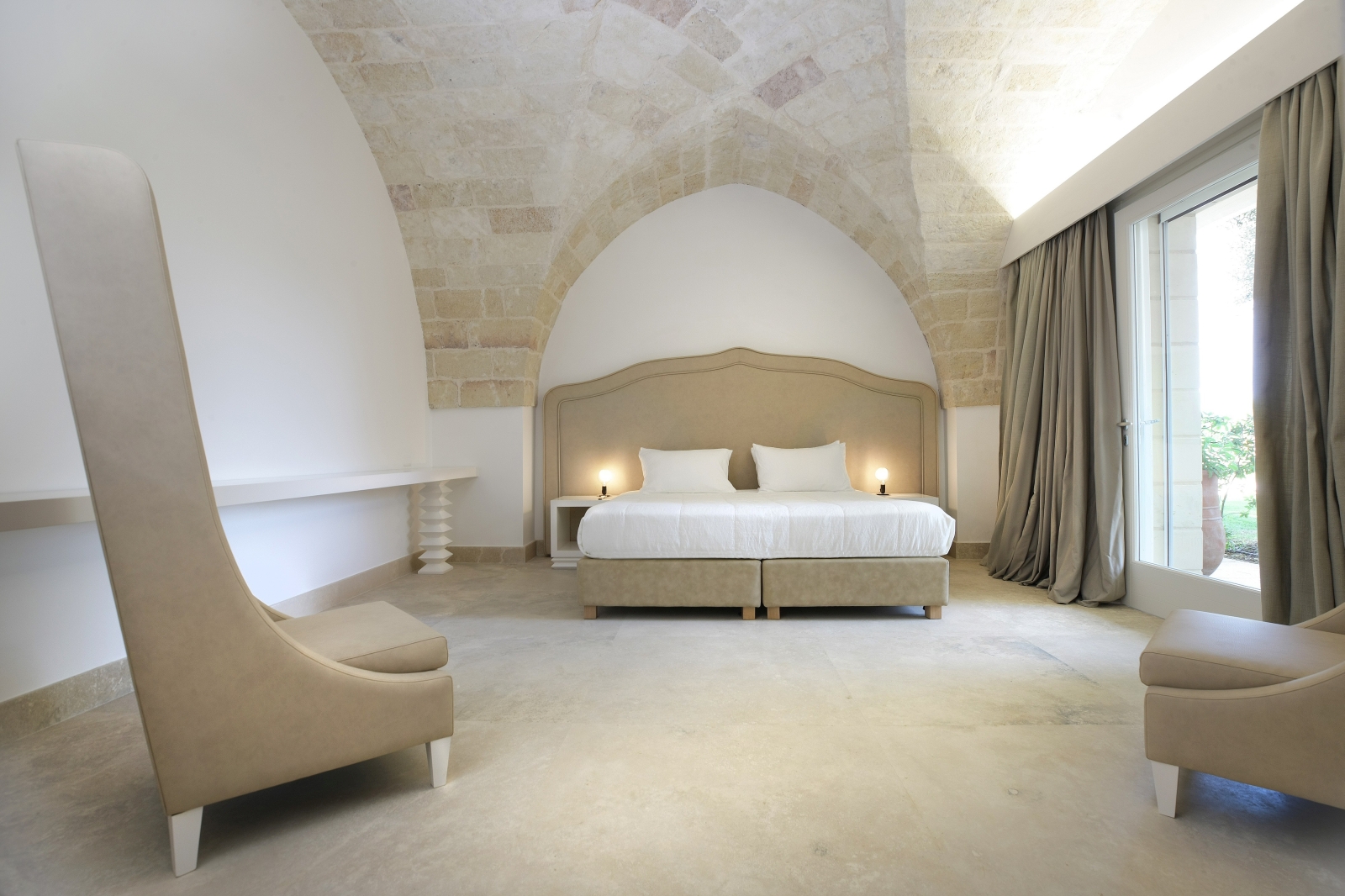 Bedroom with double bed, bedside tables, lamps, armchairs and French doors at Masseria dei Papi in Puglia, Italy