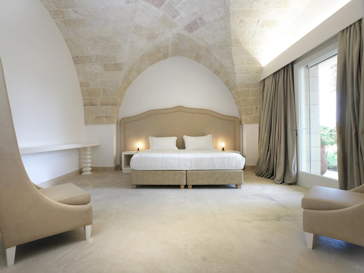 Bedroom with double bed, bedside tables, lamps, armchairs and French doors at Masseria dei Papi in Puglia, Italy