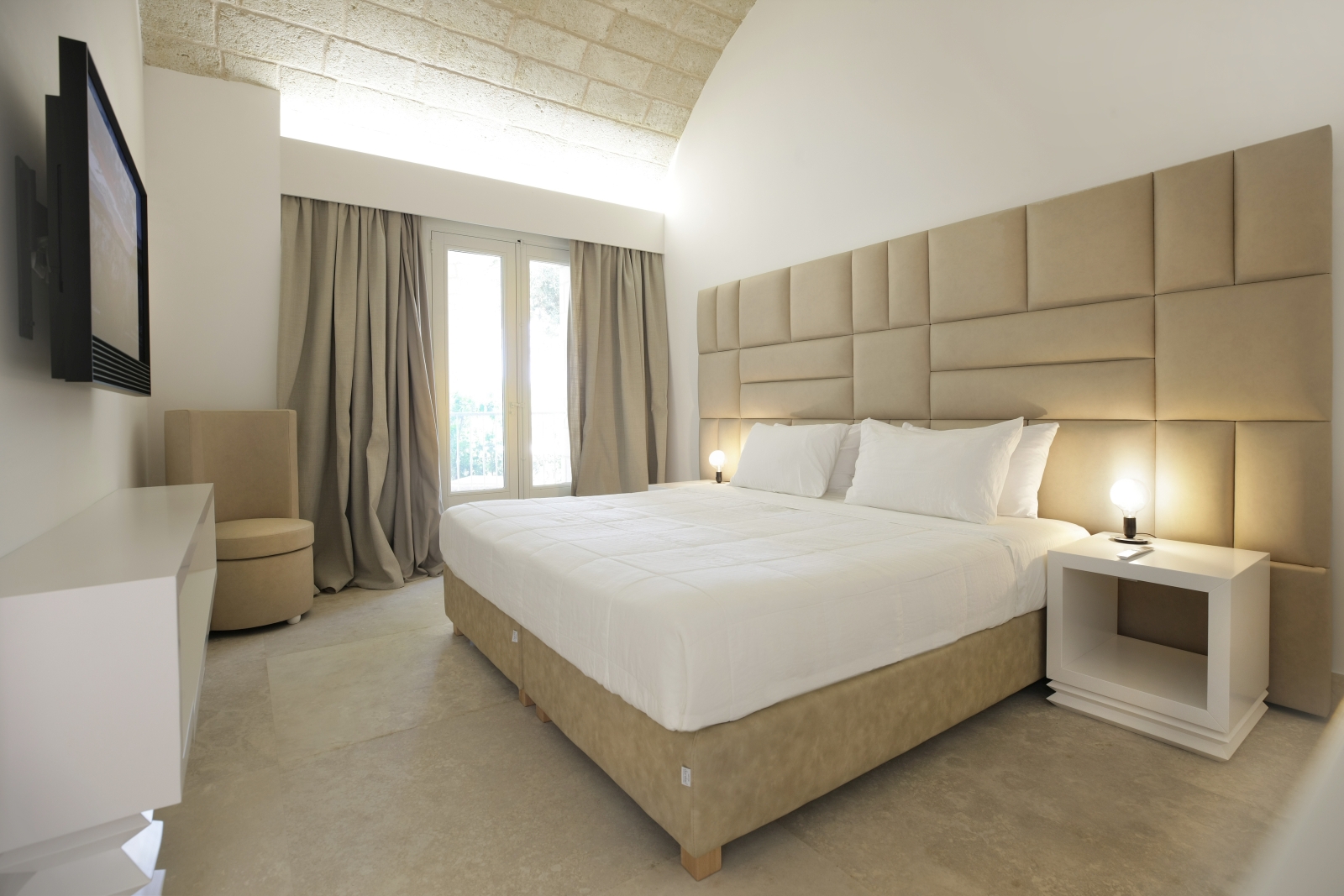 Bedroom with double bed, bedside tables, lamps, armchair, TV, armchair and French doors at Masseria dei Papi in Puglia, Italy