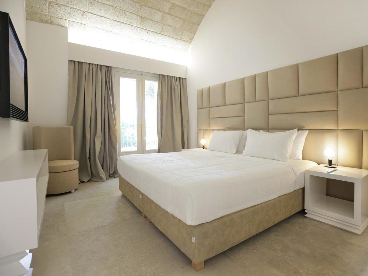 Bedroom with double bed, bedside tables, lamps, armchair, TV, armchair and French doors at Masseria dei Papi in Puglia, Italy