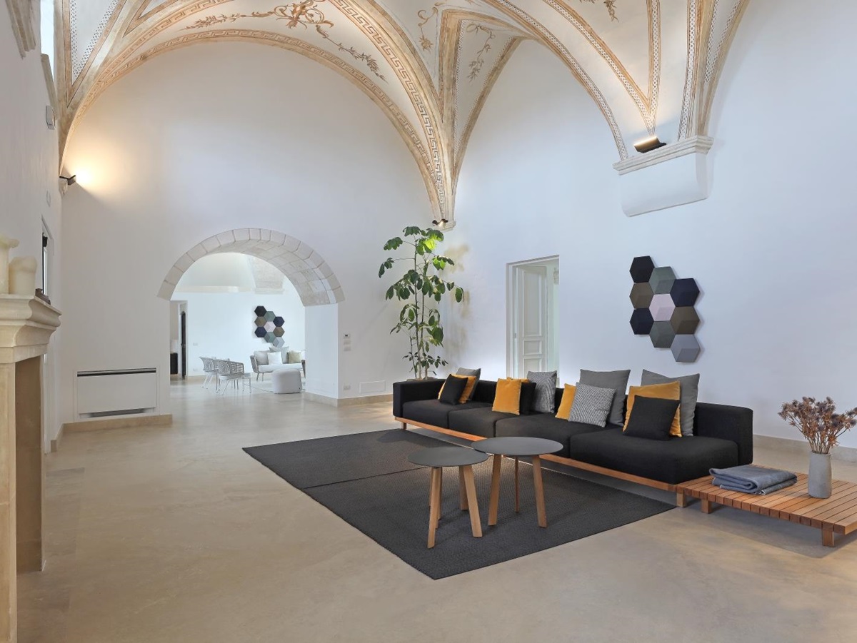 Living room with long sofa, tables, fireplace and vaulted ceiling at Masseria dei Papi in Puglia, Italy
