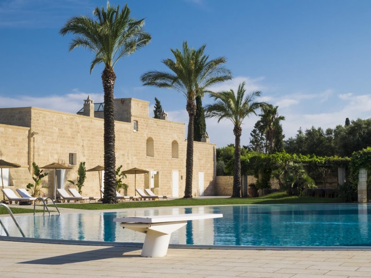 Pool with diving board and patio area with sun loungers, umbrellas and palm trees at Masseria dei Papi in Puglia, Italy