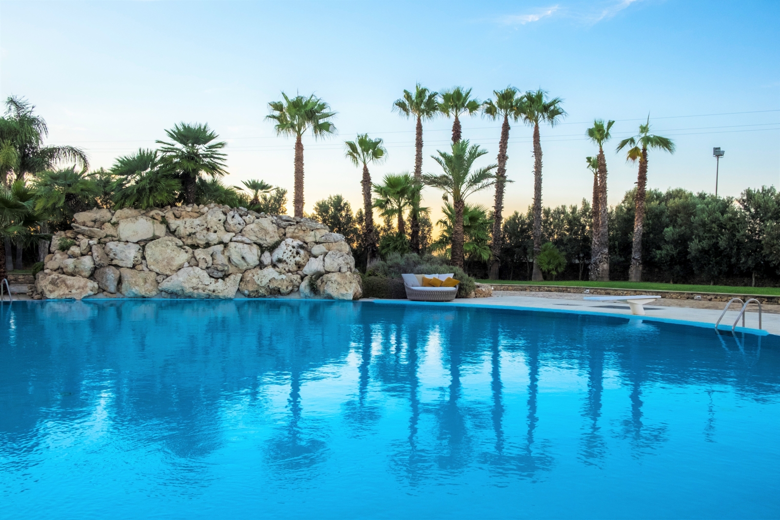 Pool and patio with sofa, diving board and palm trees at Masseria dei Papi in Puglia, Italy