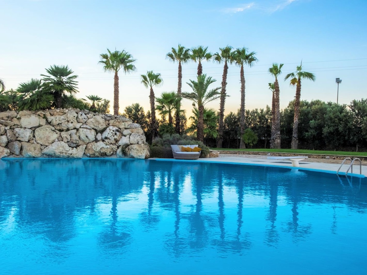 Pool and patio with sofa, diving board and palm trees at Masseria dei Papi in Puglia, Italy