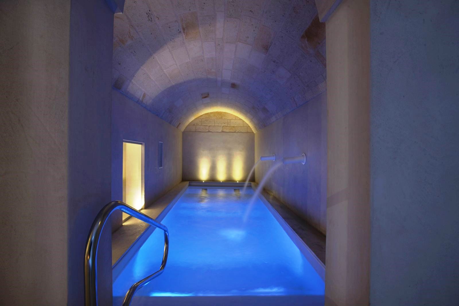 Indoor pool in spa with curved stone ceiling and 2 water fountains coming out of wall at villa masseria dei papi in Puglian, Italy